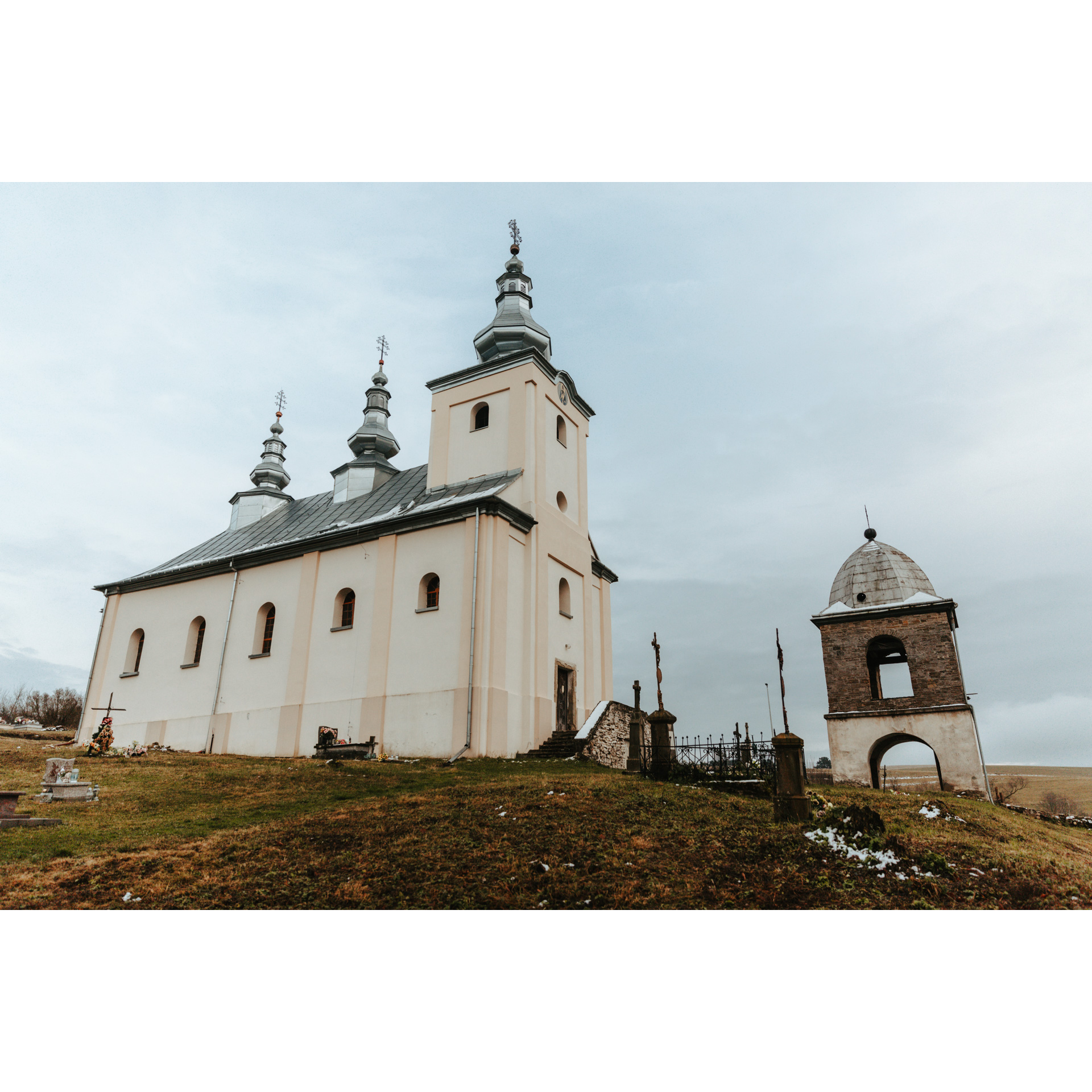 A bright brick Orthodox church with three turrets with a bell tower next to it against the sky