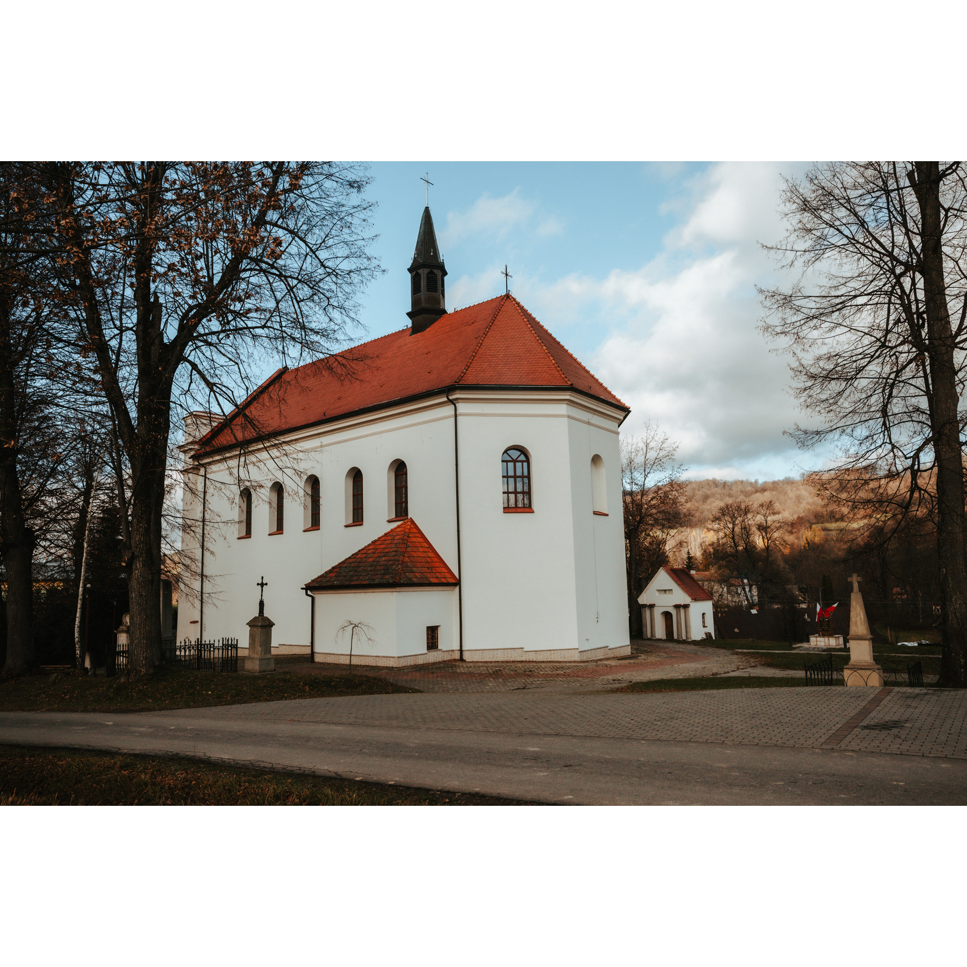 A large white church with a red roof among the trees against the hills