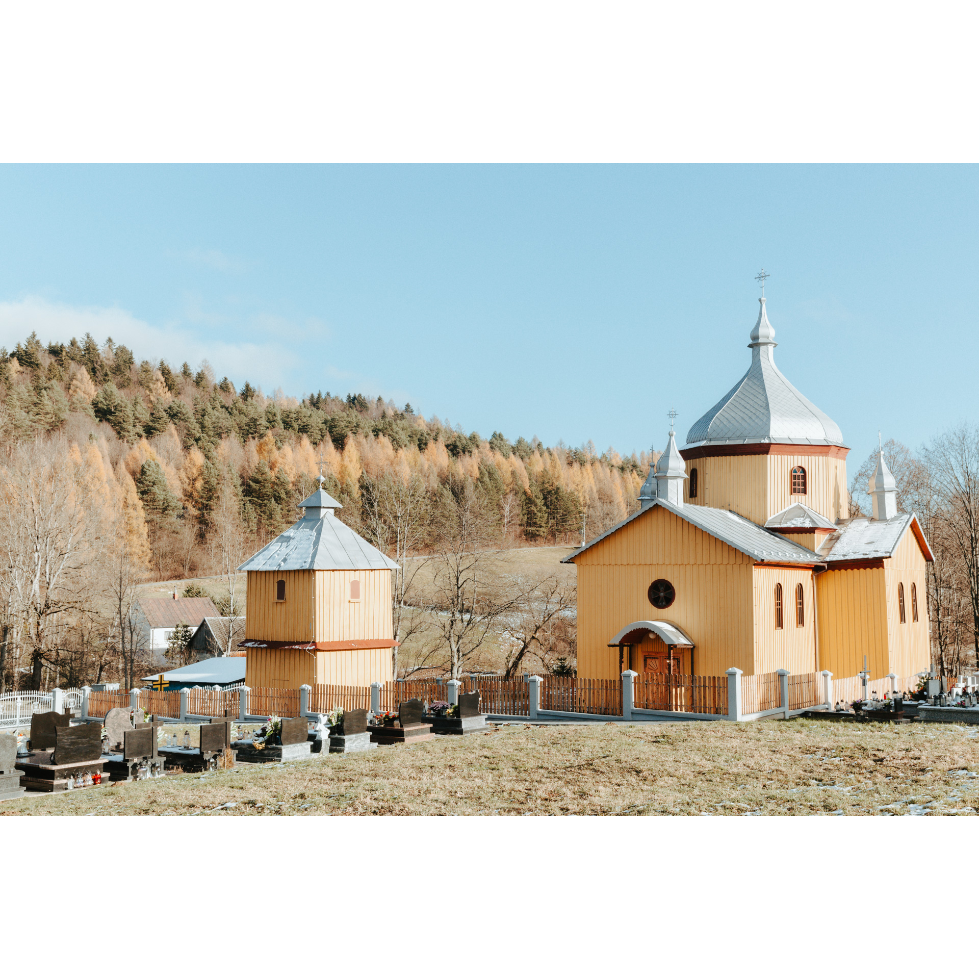 A wooden church with a gray roof with a bell tower and a cemetery in front