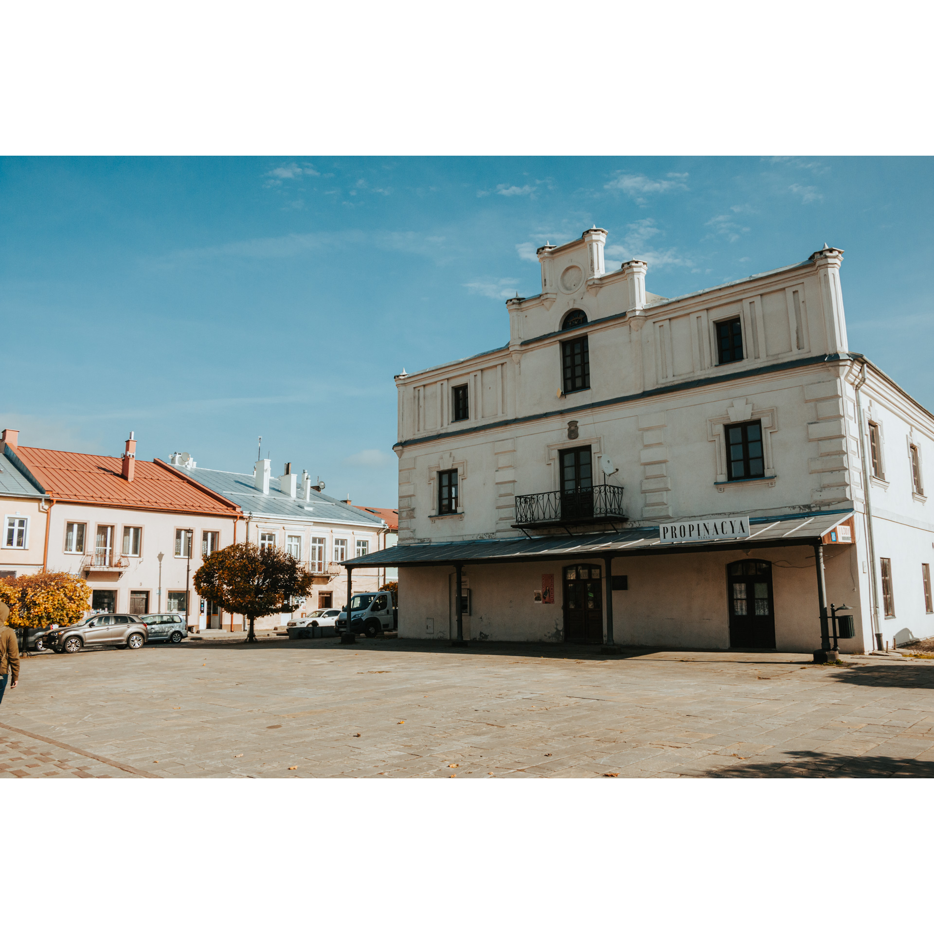 Jasny budynek ratusza w centrum rynku z zadaszeniem nad wejściem, balkonem i ozdobną fasadą