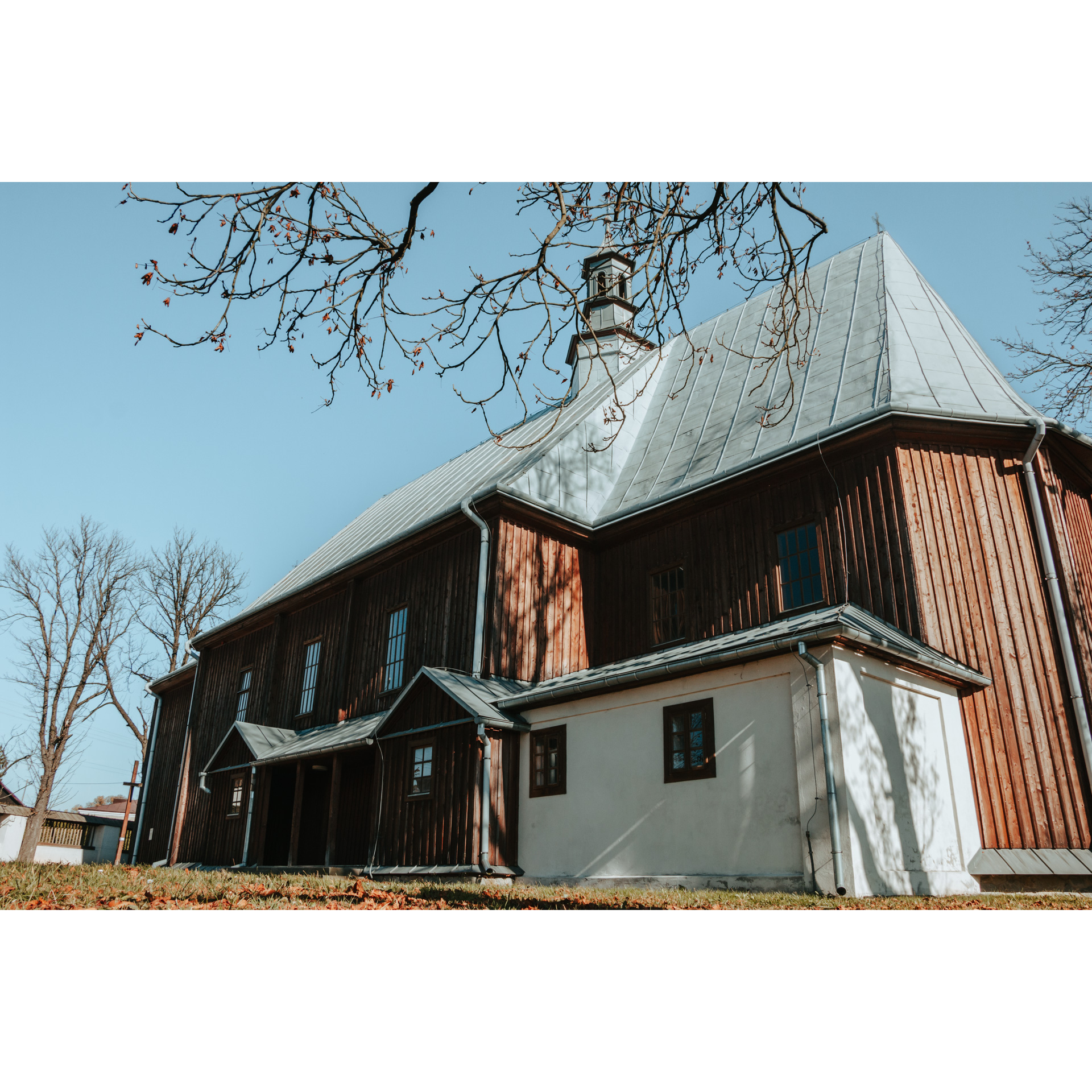 View of the side wall of a tall wooden church with a gray roof and a white brick outbuilding