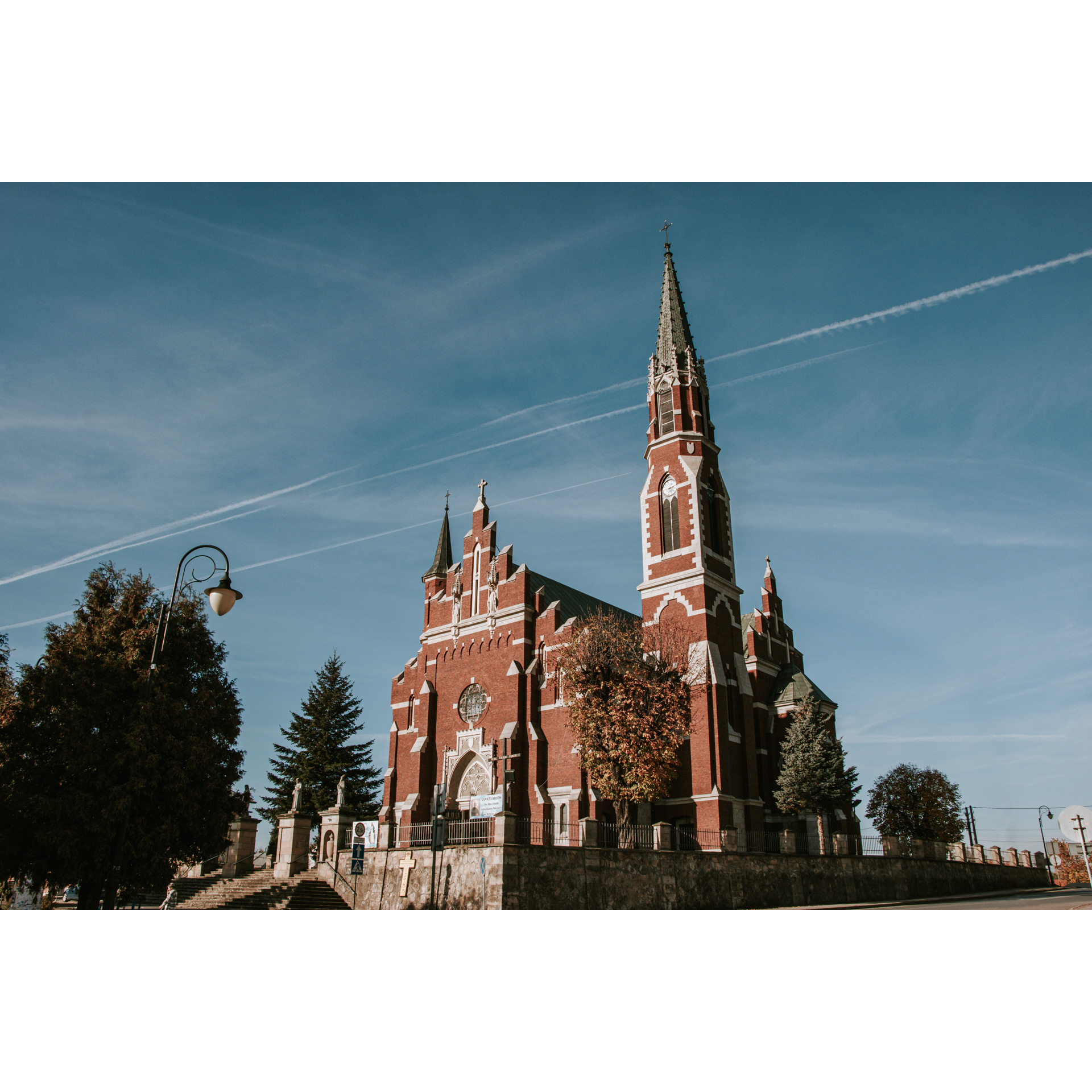 Duży ceglany kościół z białymi wykończeniami, schodkową fasadą oraz ze strzelistymi, wysokimi wieżami 