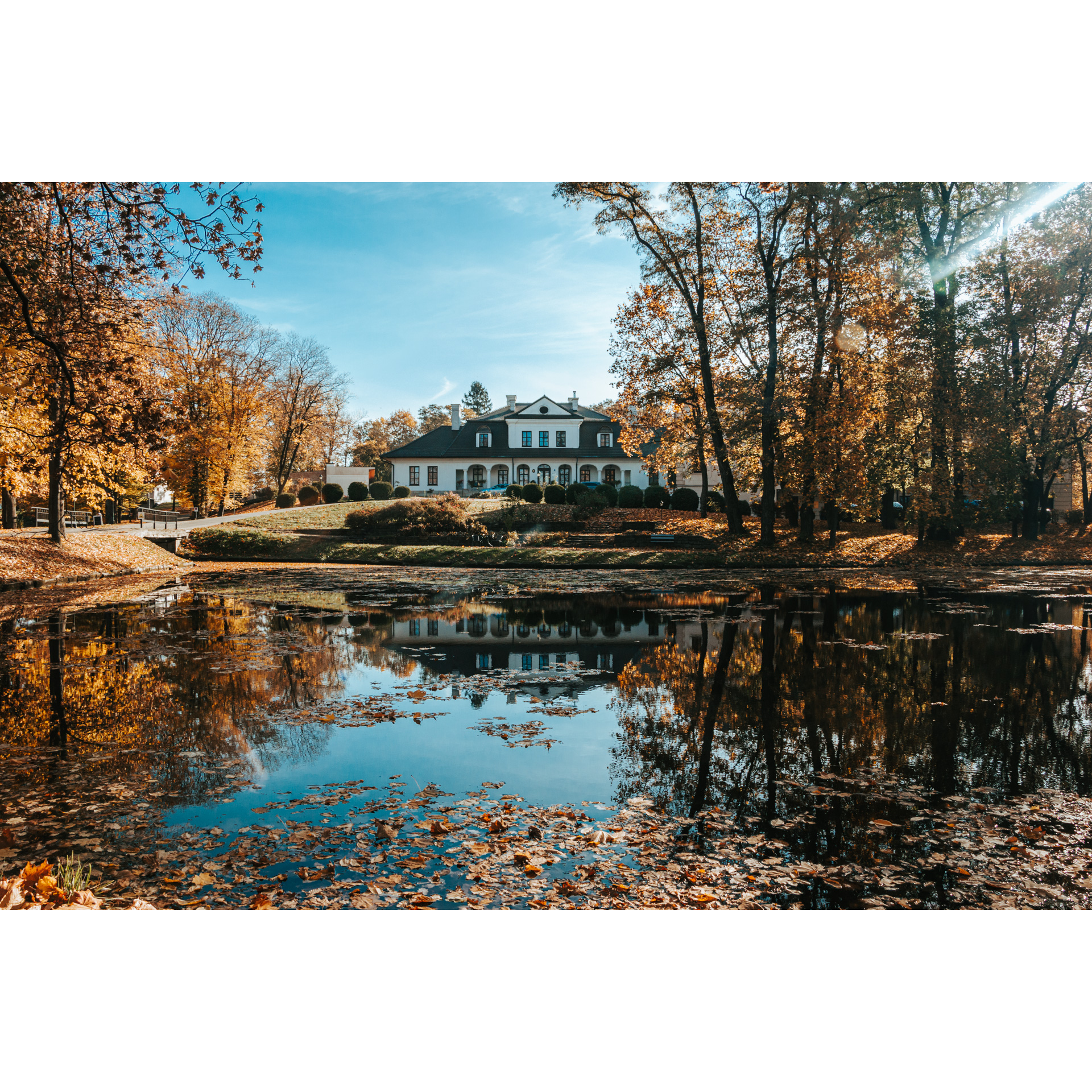 A view of a white manor house from behind a large pond among autumn trees