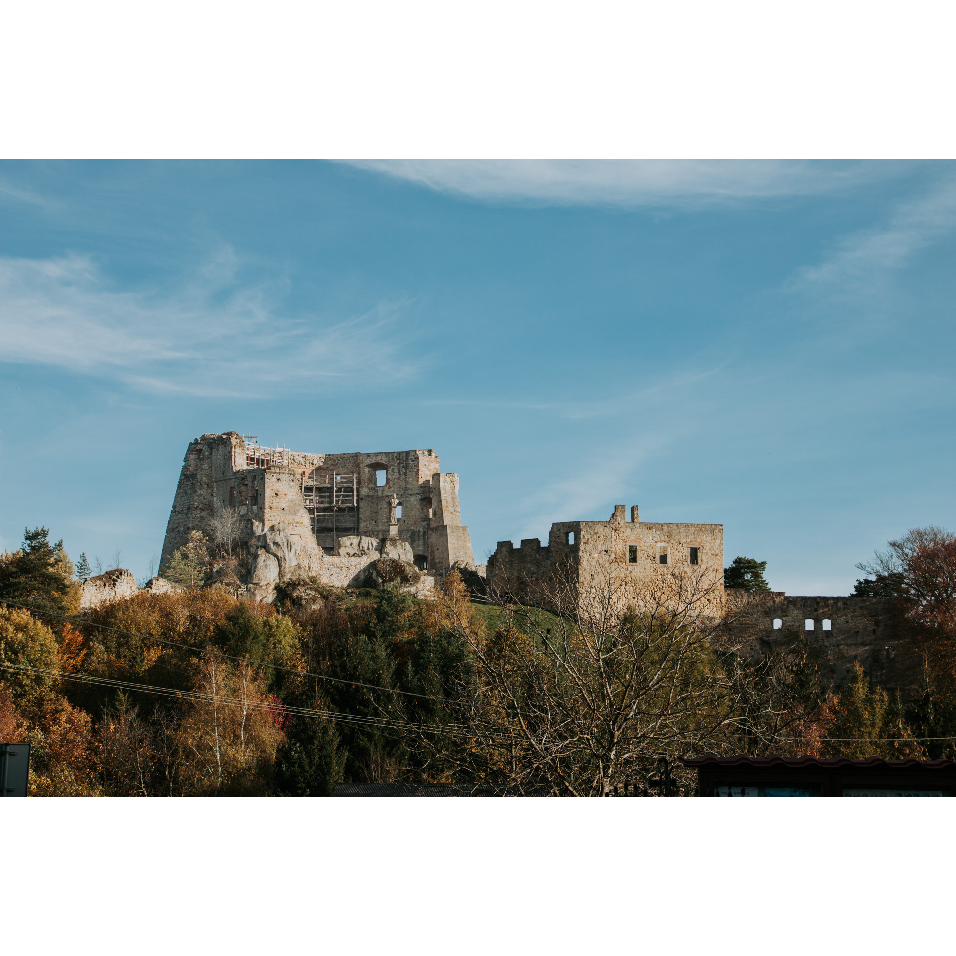 Widok na ruiny zamku na zalesionym wzgórzu na tle niebieskiego nieba