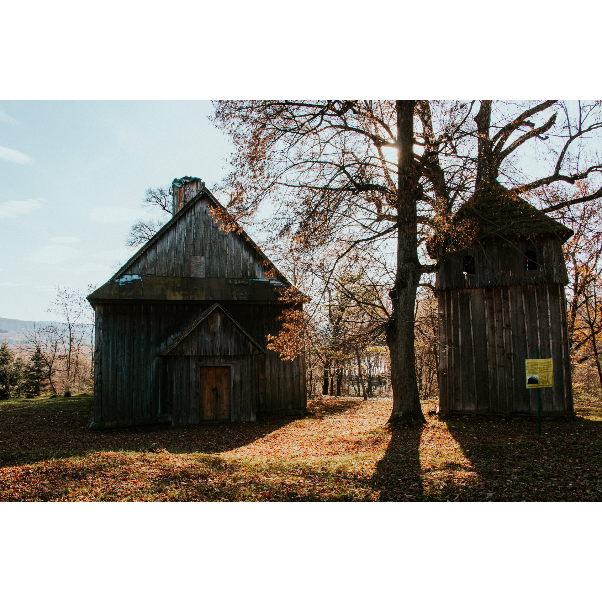 An old wooden church next to a bell tower and a tree