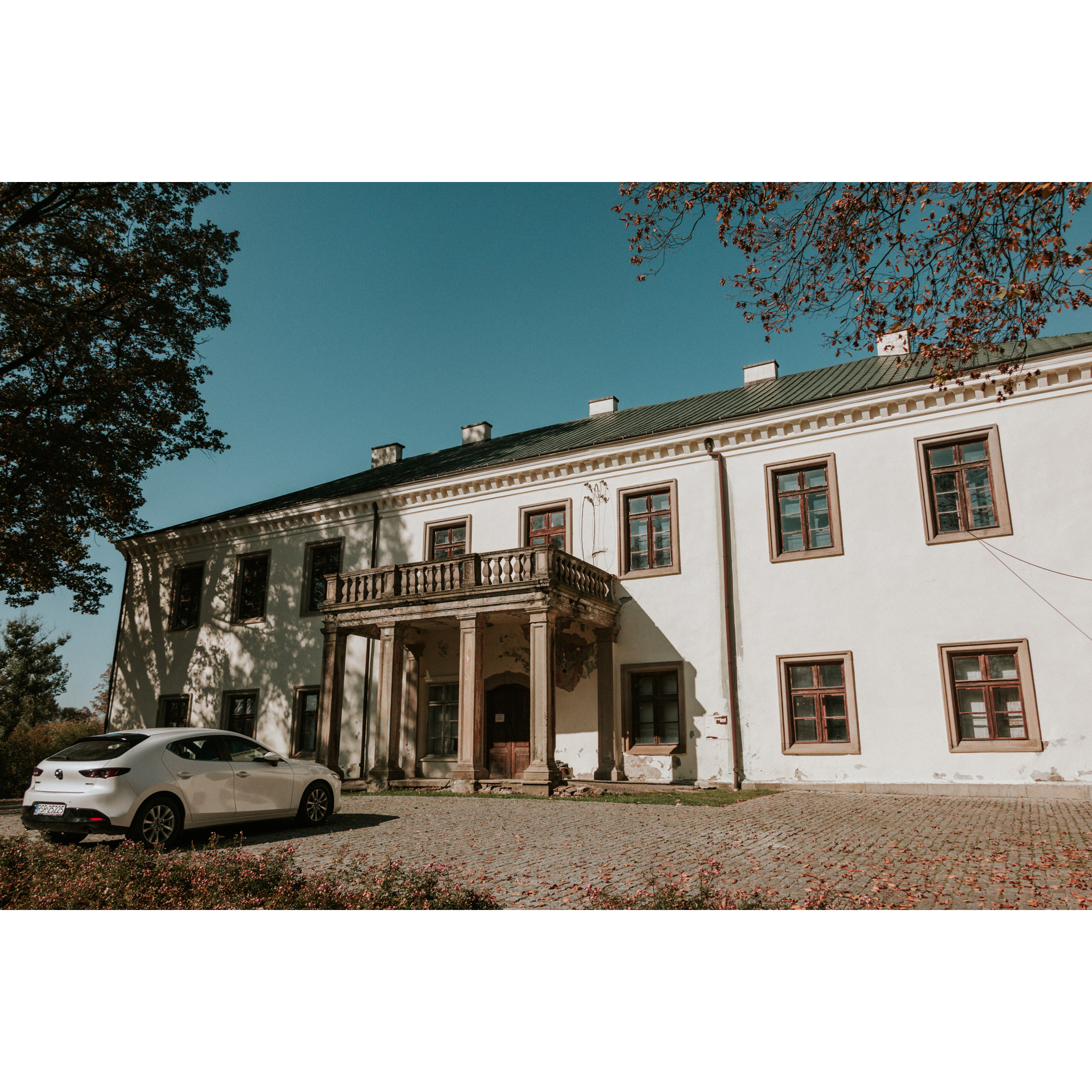 A large bright manor house with a balcony above the entrance supported by columns