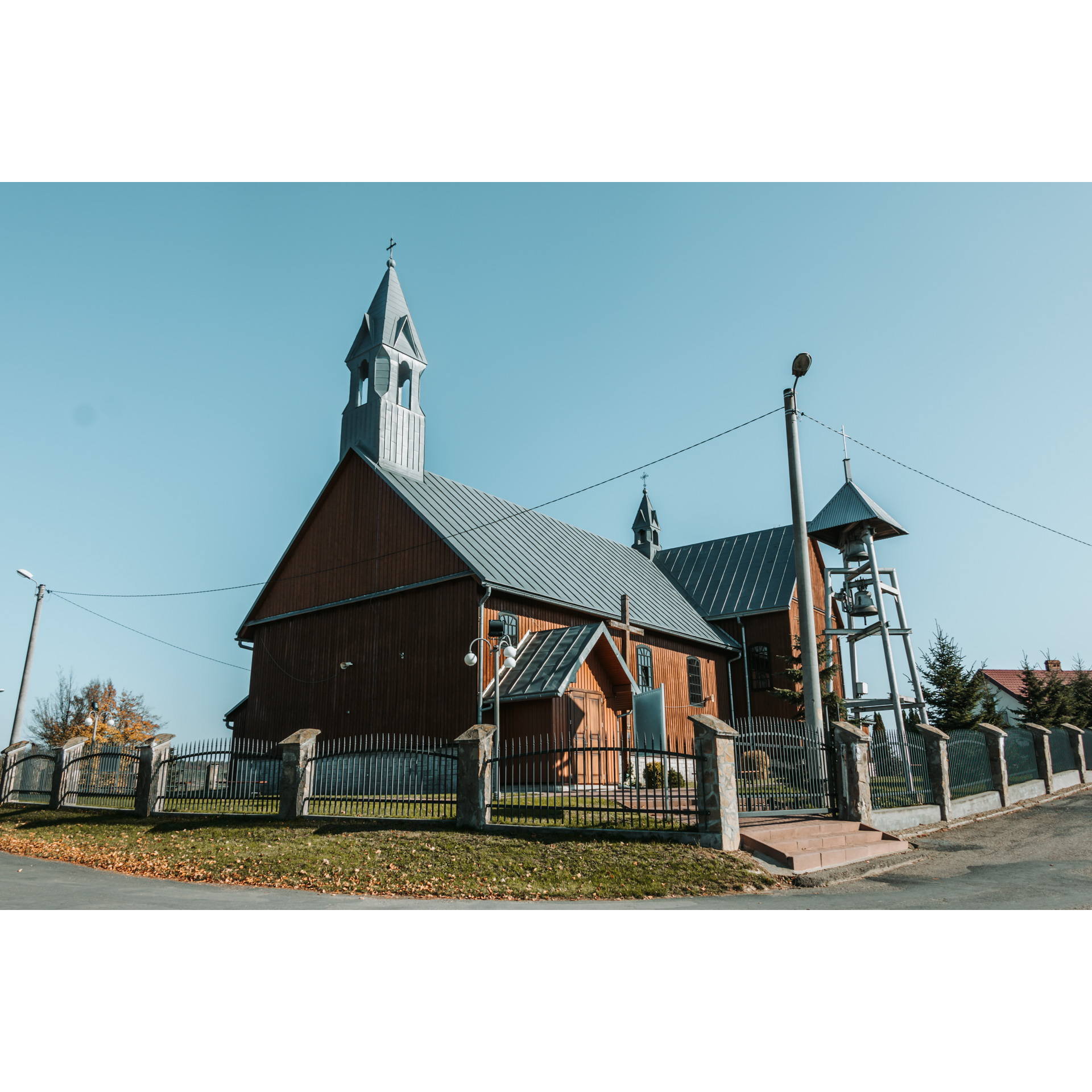 Drewniany kościół z wieżyczką i dzwonnicą otoczony metalowym płotem