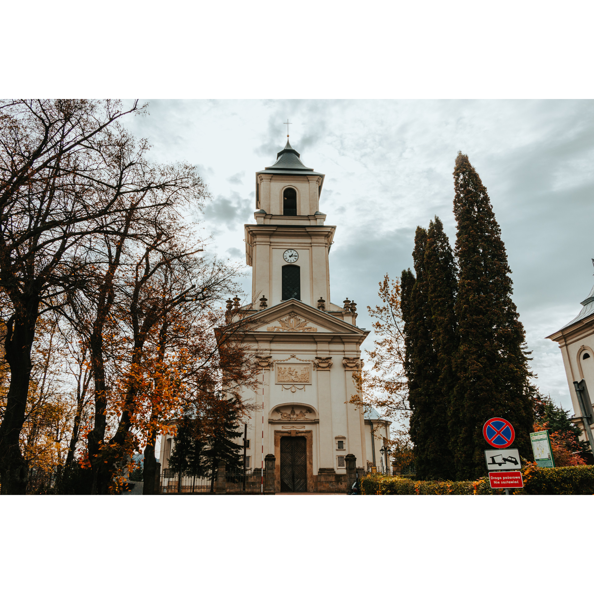 Wejście do murowanego kościoła z wysoką wieżą z zegarem i kopułą