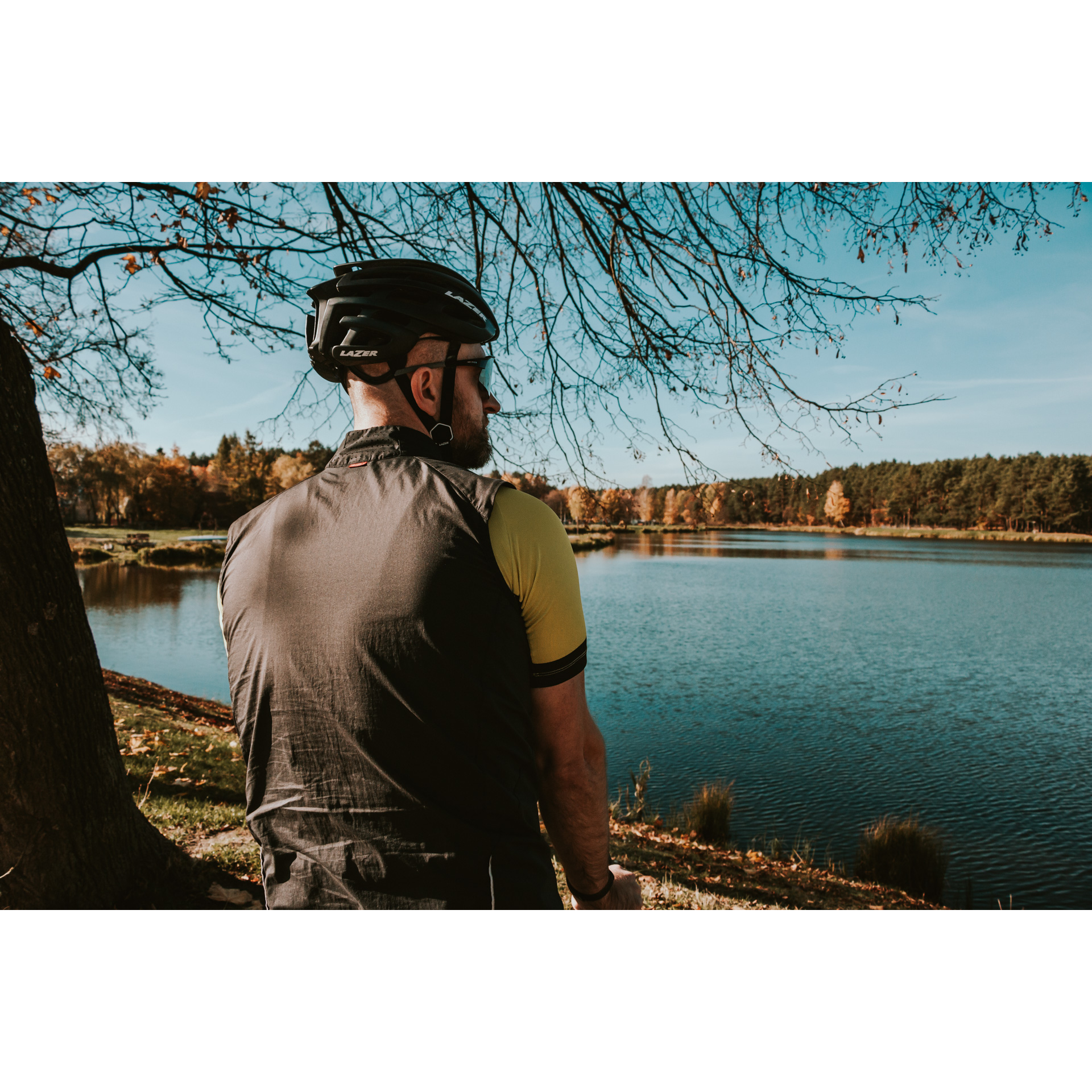 Rowerzysta w kasku i szarej koszulce patrzący na zalew wodny 