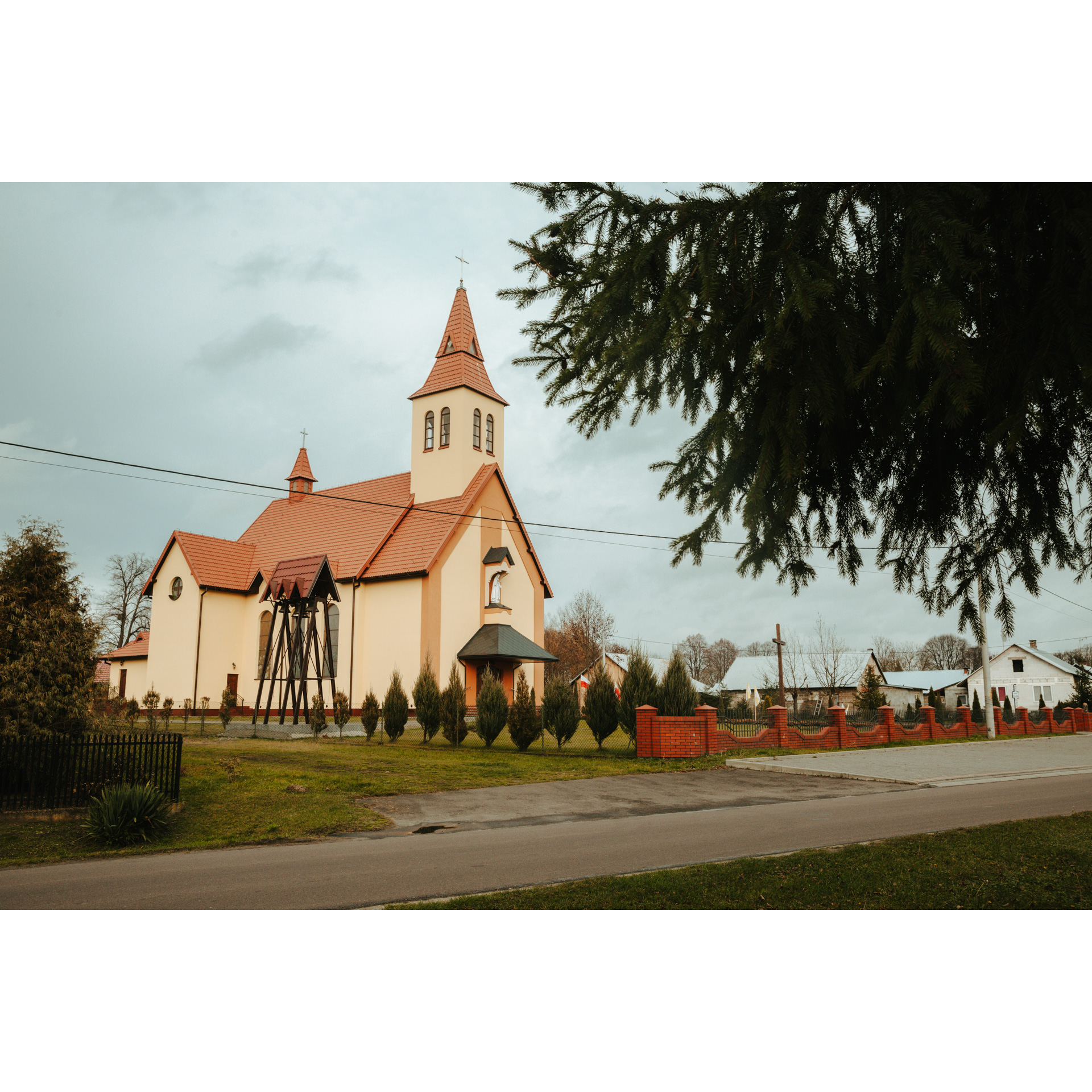 An orange church with a red roof and a tall steeple behind a dark green tree