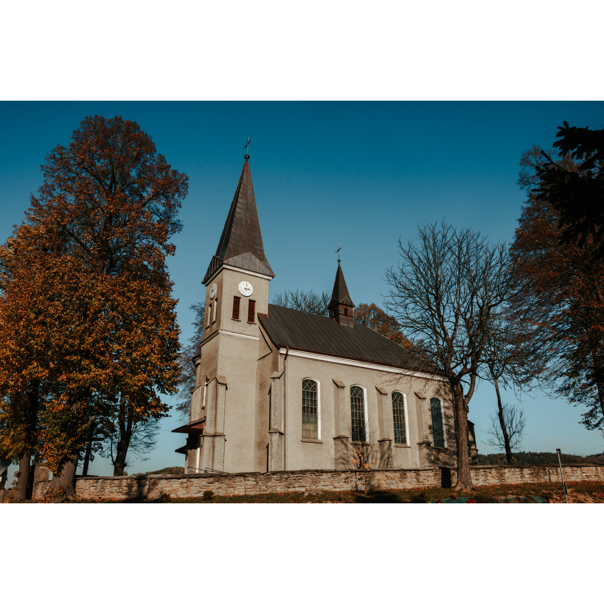 Jasny kościół ze strzelistą wieżą obok jesiennych drzew