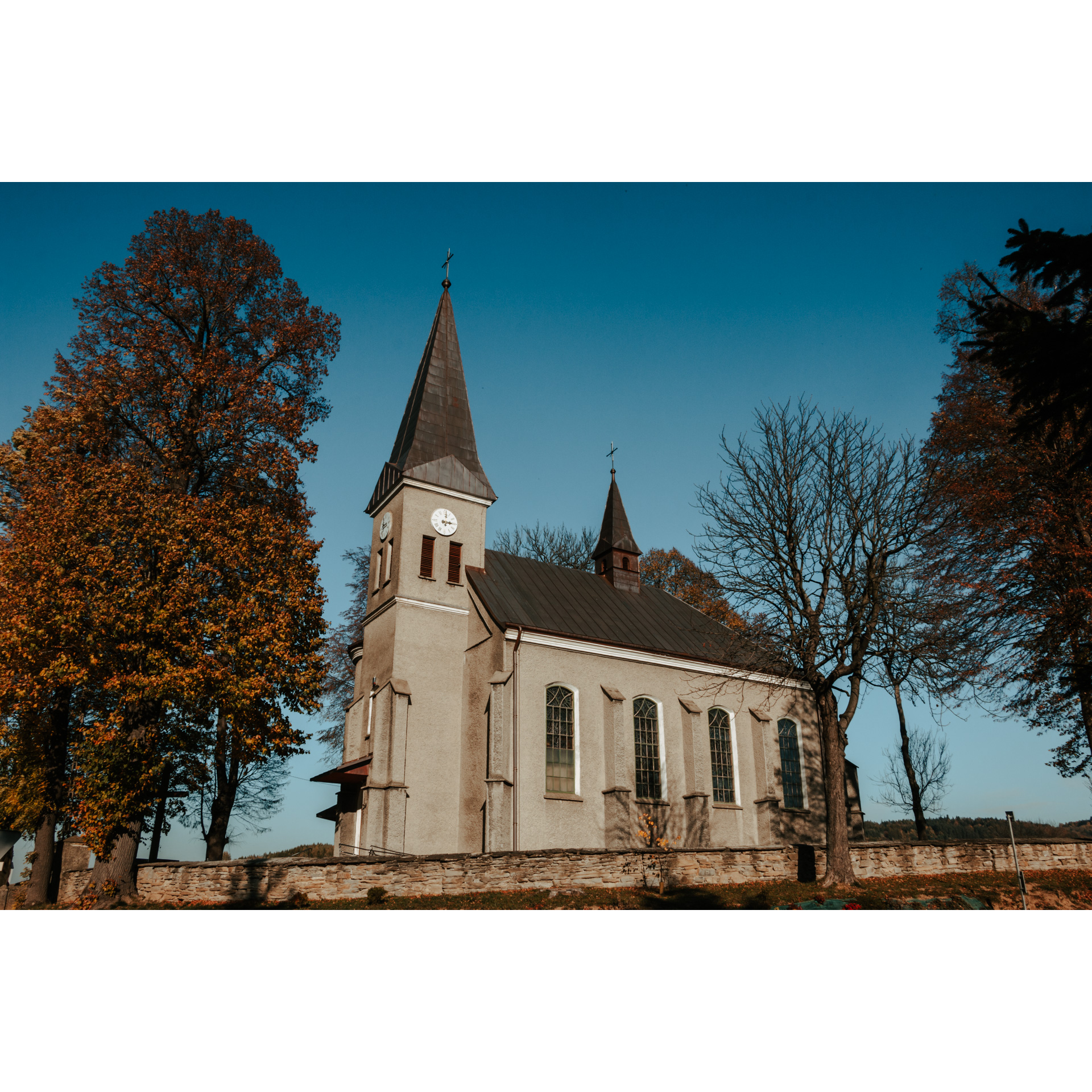 A bright church with a soaring tower next to autumn trees