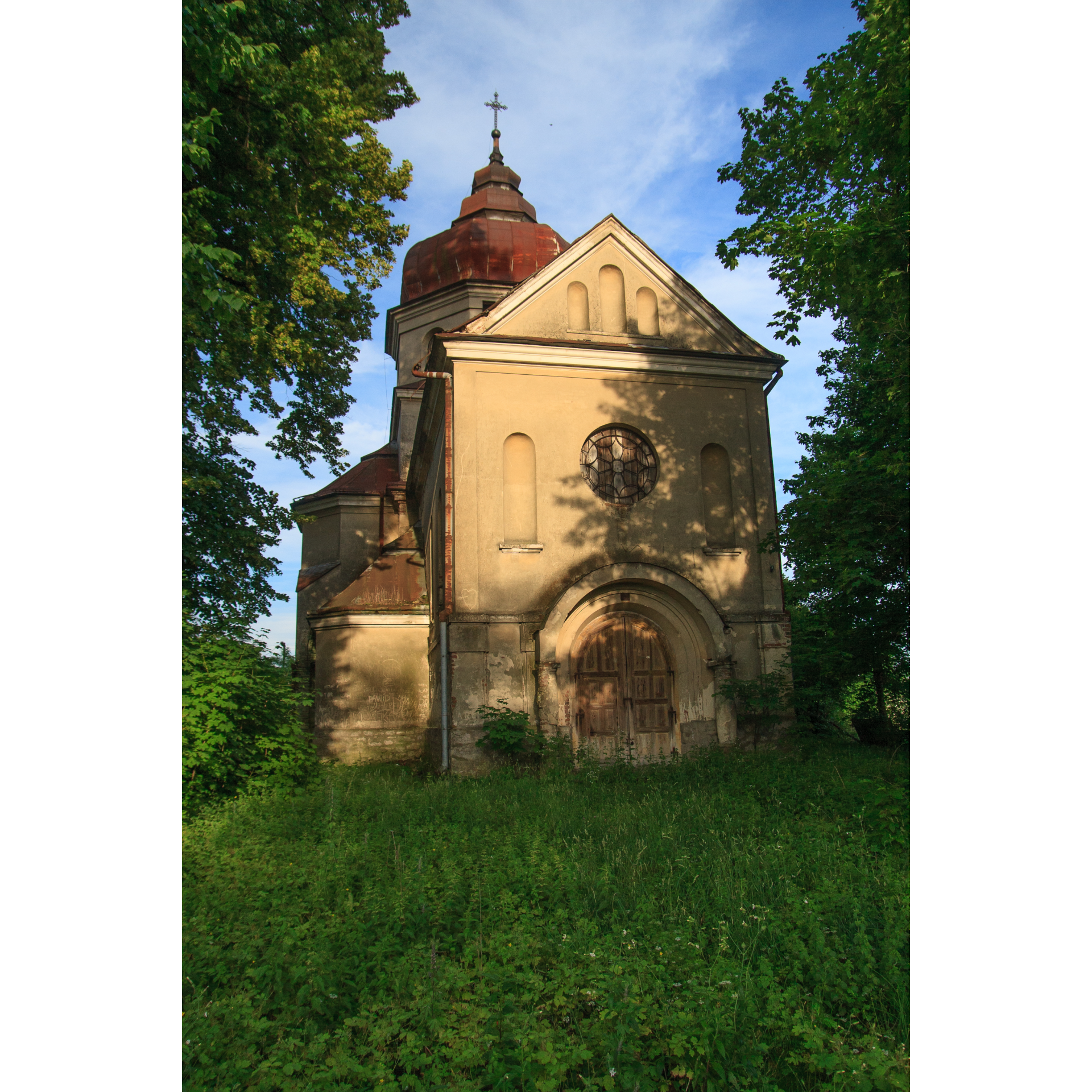 A bright, brick Orthodox church with a wooden door and a round stained-glass window