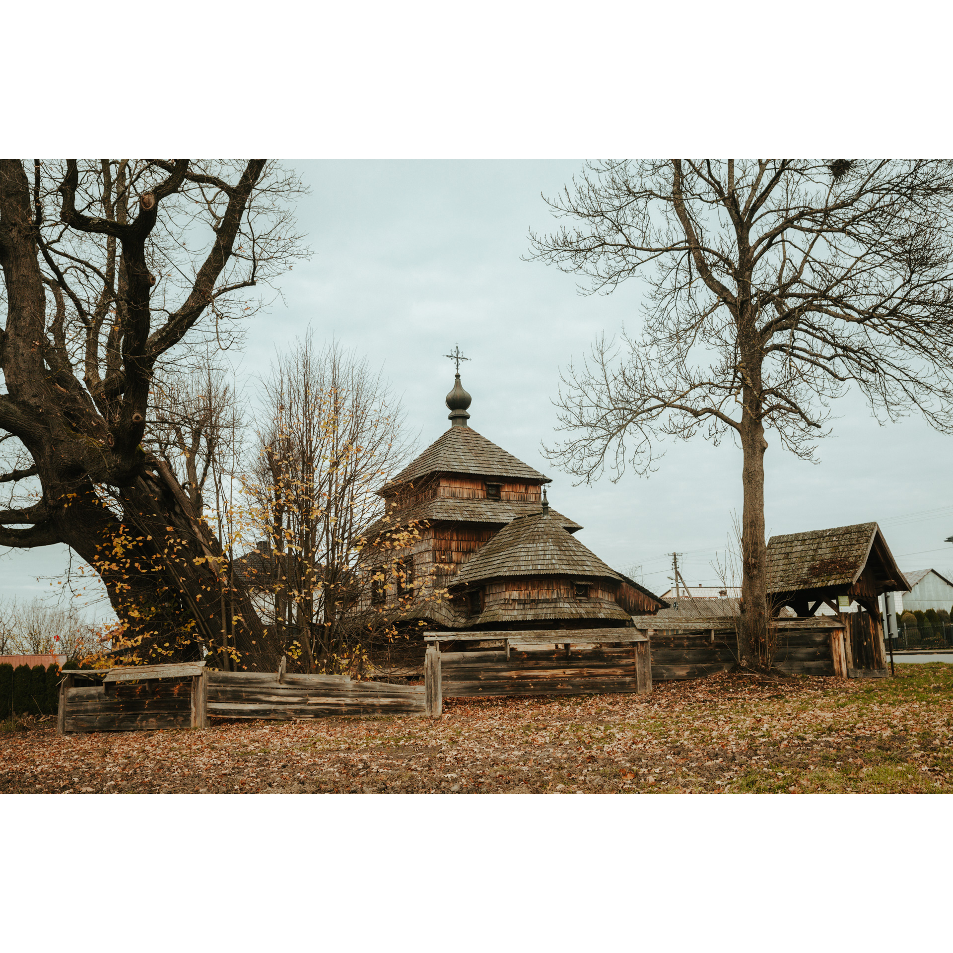 Drewniana cerkiew otoczona drewnianym płotem wśród drzew