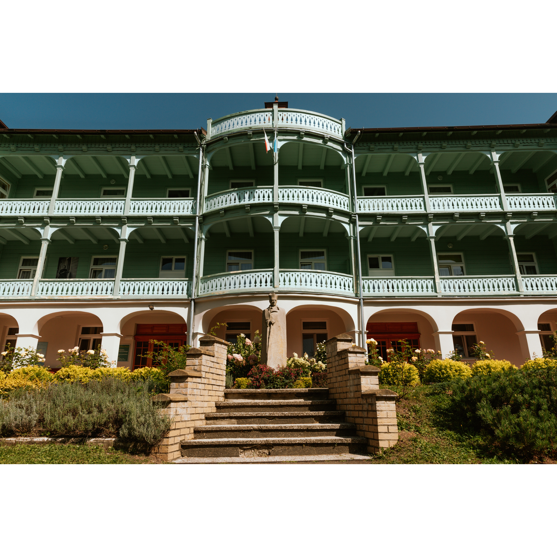 A three-story building with a wide front with doors shaded by a balcony supported by seven columns, each floor has a balcony at the front