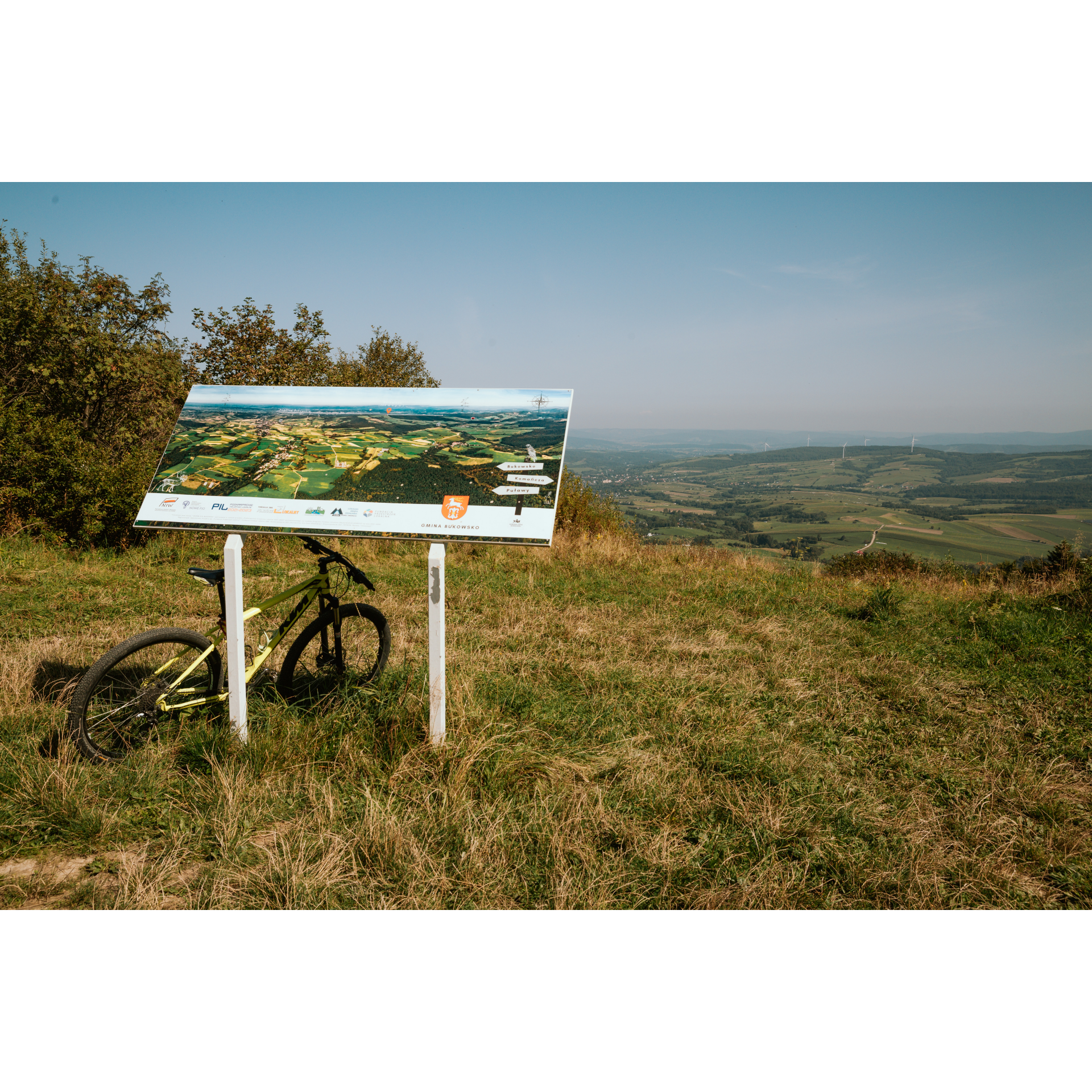 A bicycle leaning on an information board located on a hill, with a view of the valley in the background