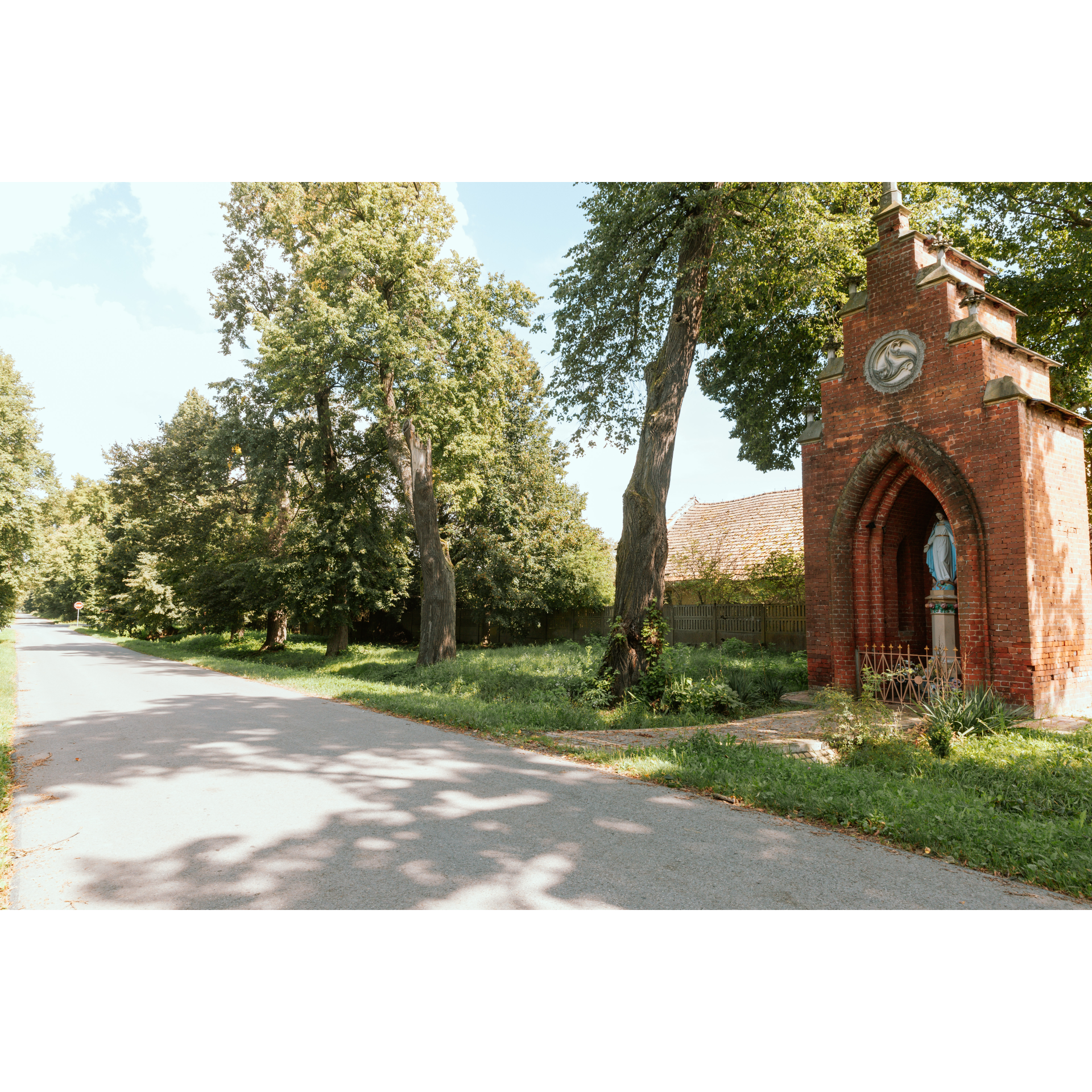 A chapel standing by the road, built of red brick with a slender shape and a figure of the Virgin Mary.