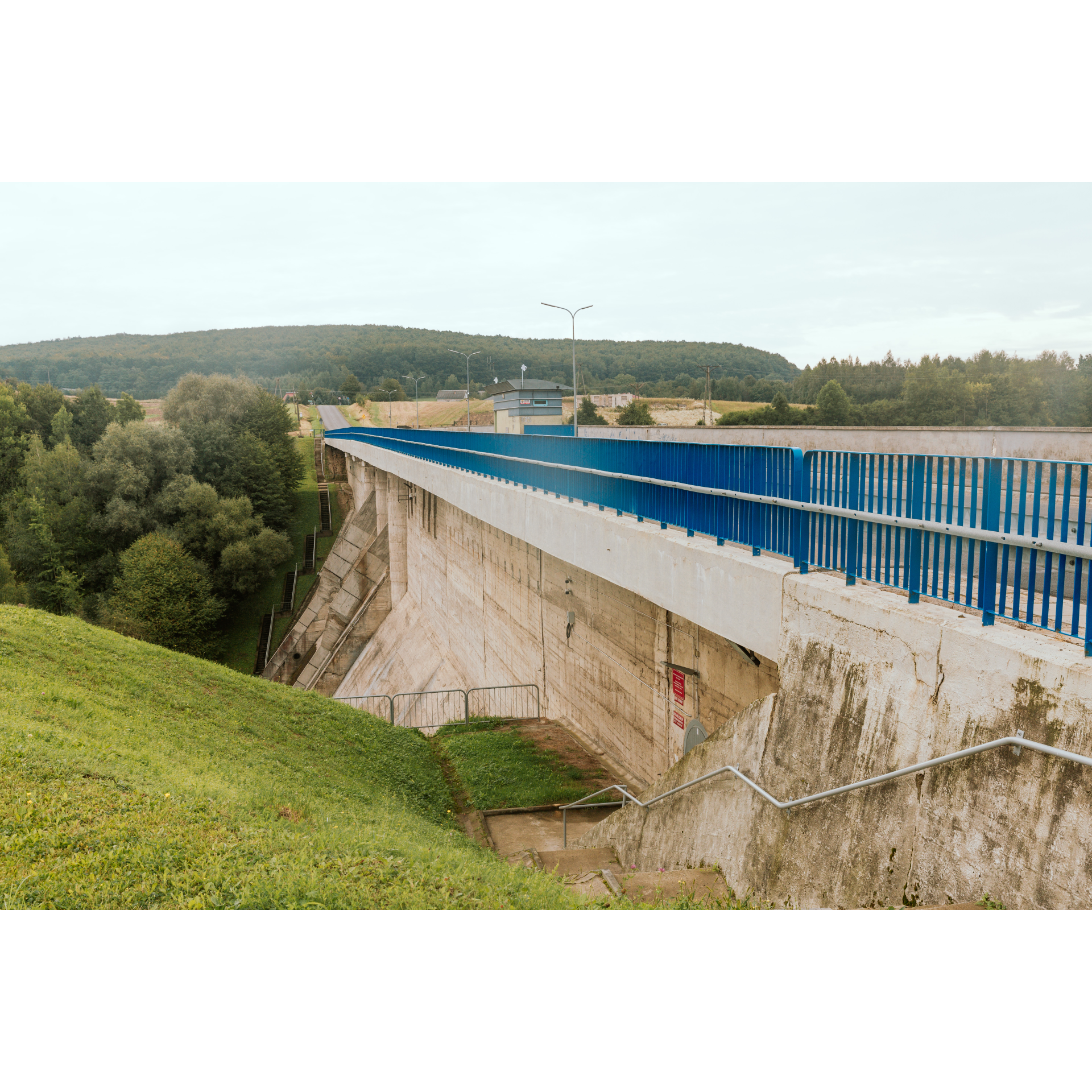 Concrete dam and blue bridge, green vegetation on the left