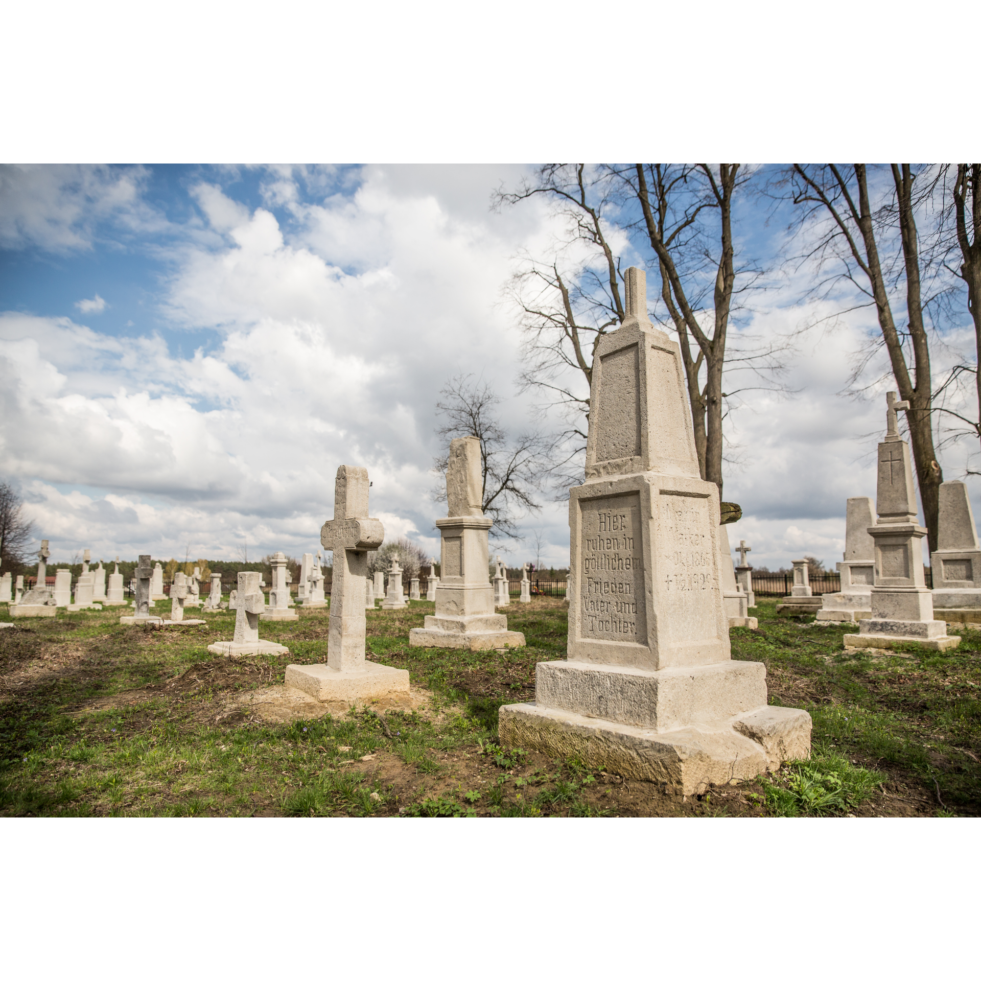 Bright stone memorials and cemetery crosses with German inscriptions against a blue sky with clouds