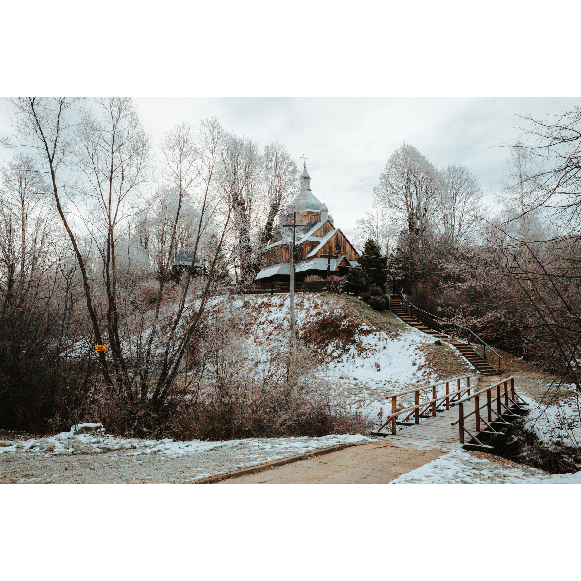 A wooden church with a bright roof on a snow-covered hill, accessed by wooden stairs