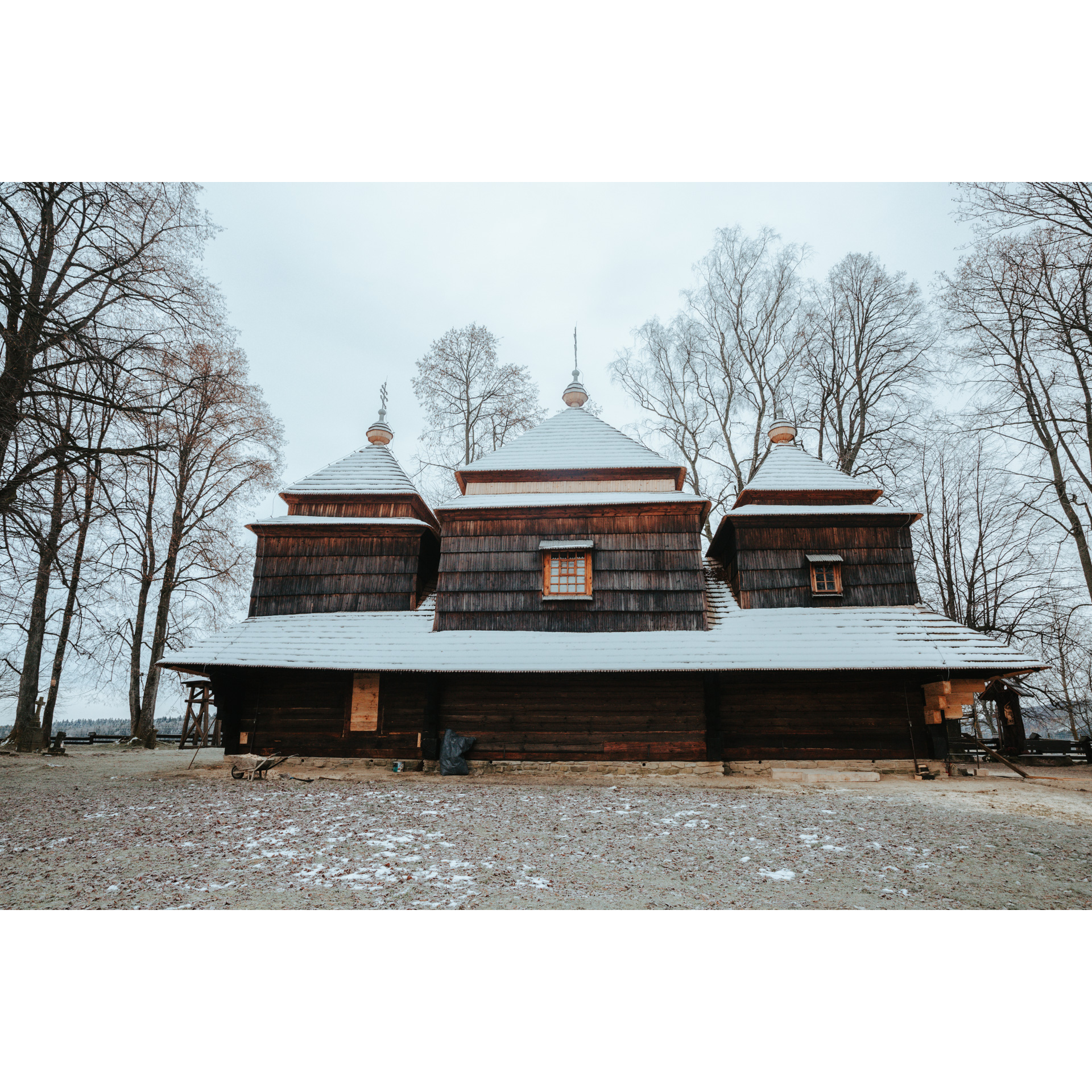Wooden Orthodox church with a snow-covered roof and a large window among the trees