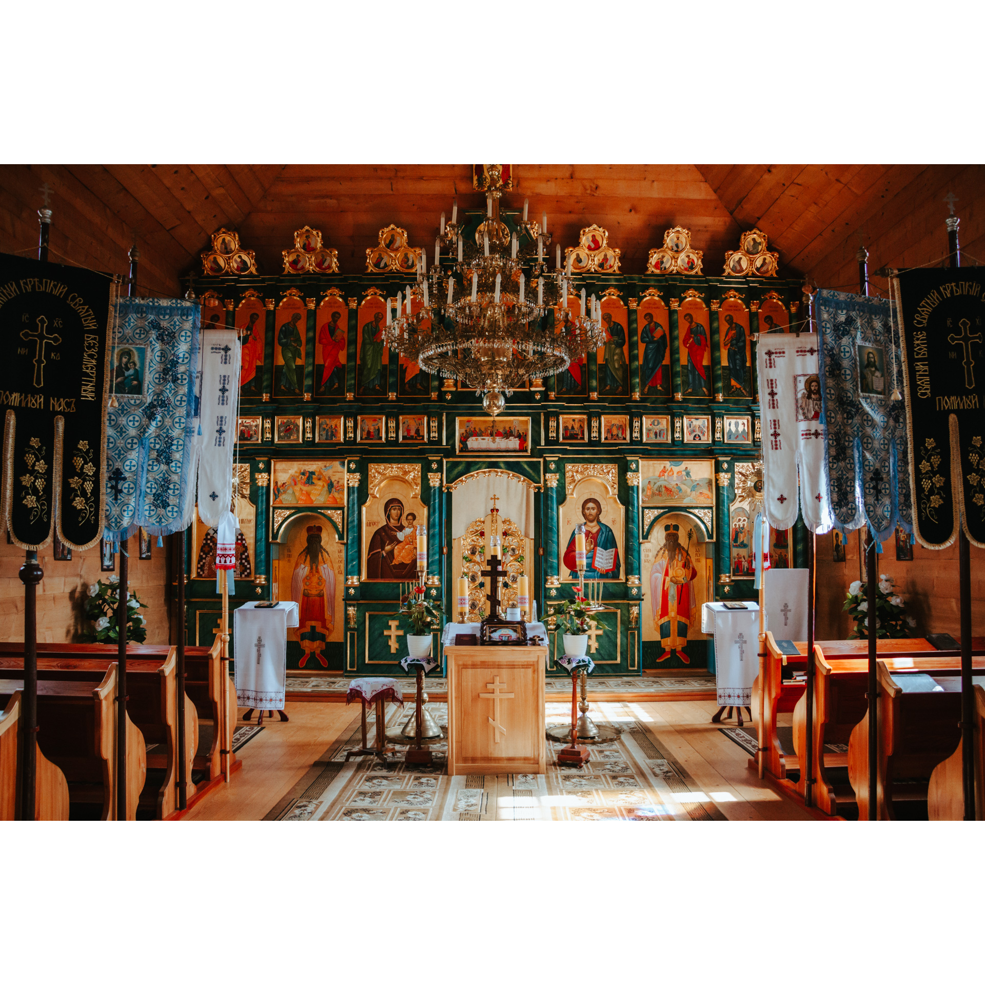 The altar of a wooden church with an iconostasis, a hanging crystal chandelier and wooden benches on the sides