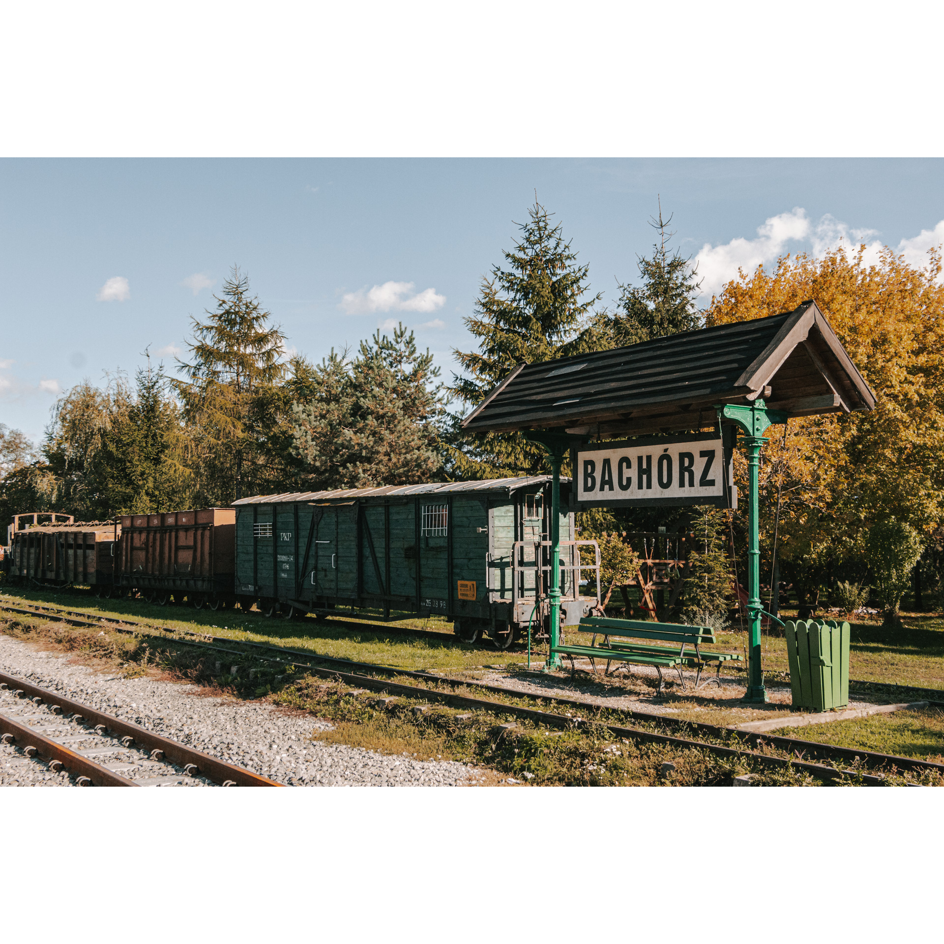 An information sign placed on green supports, covered with a wooden roof, in the background green and brown old wagons and tracks