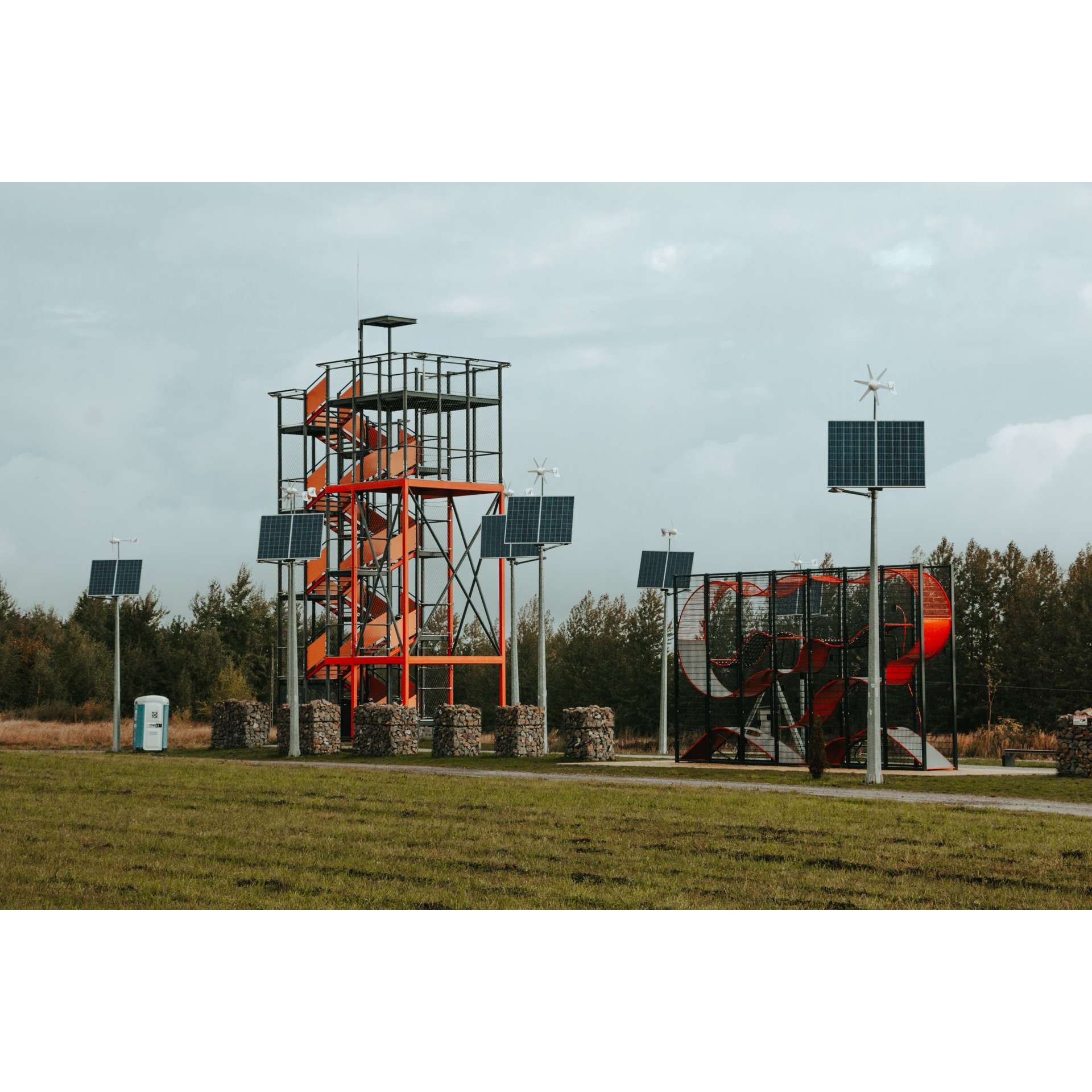 A viewing platform built of black metal scaffolding and red steps surrounded by individual photovoltaic panels and