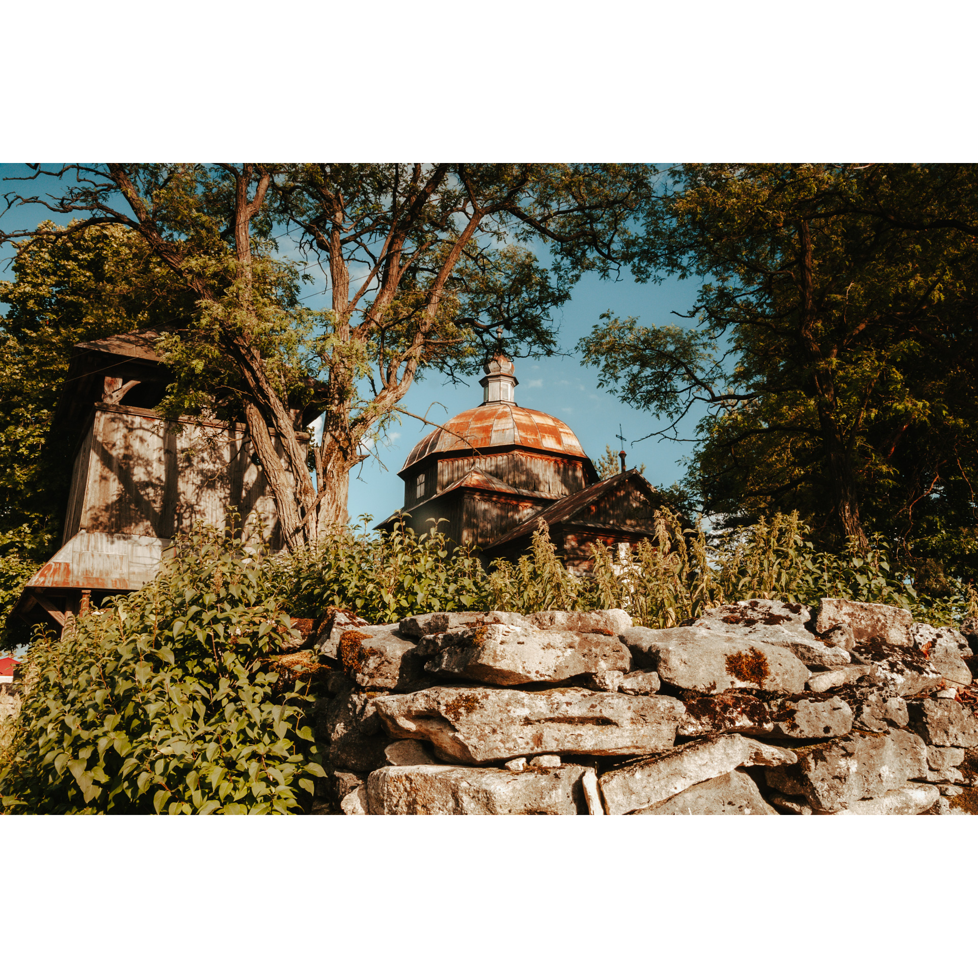 The red dome of the church among the trees seen from behind a stone wall covered with vegetation