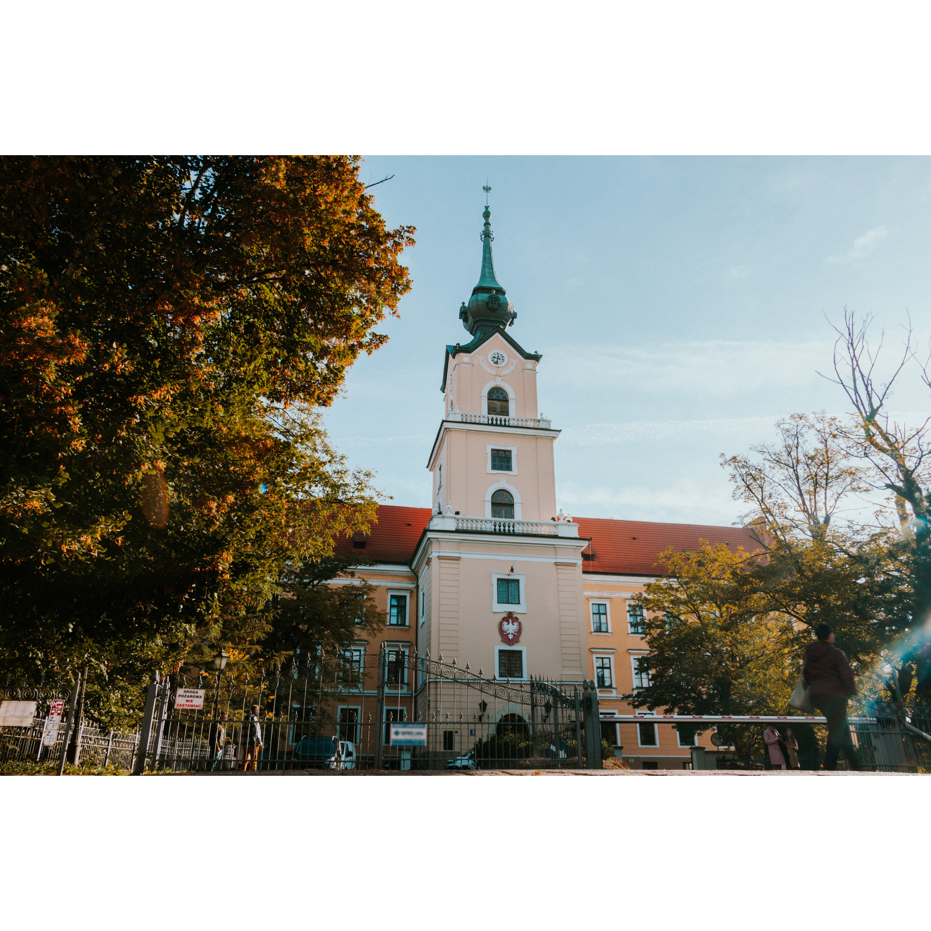 The tower of the castle with a clock and the emblem of Poland ended with a green turret among the trees