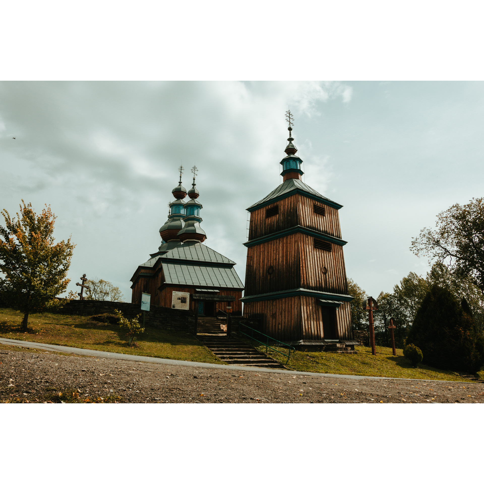 Drewniana cerkiew z dużą, wysoką dzwonnicą i kopułami, do której prowadzą kamienne schody z zieloną barierką
