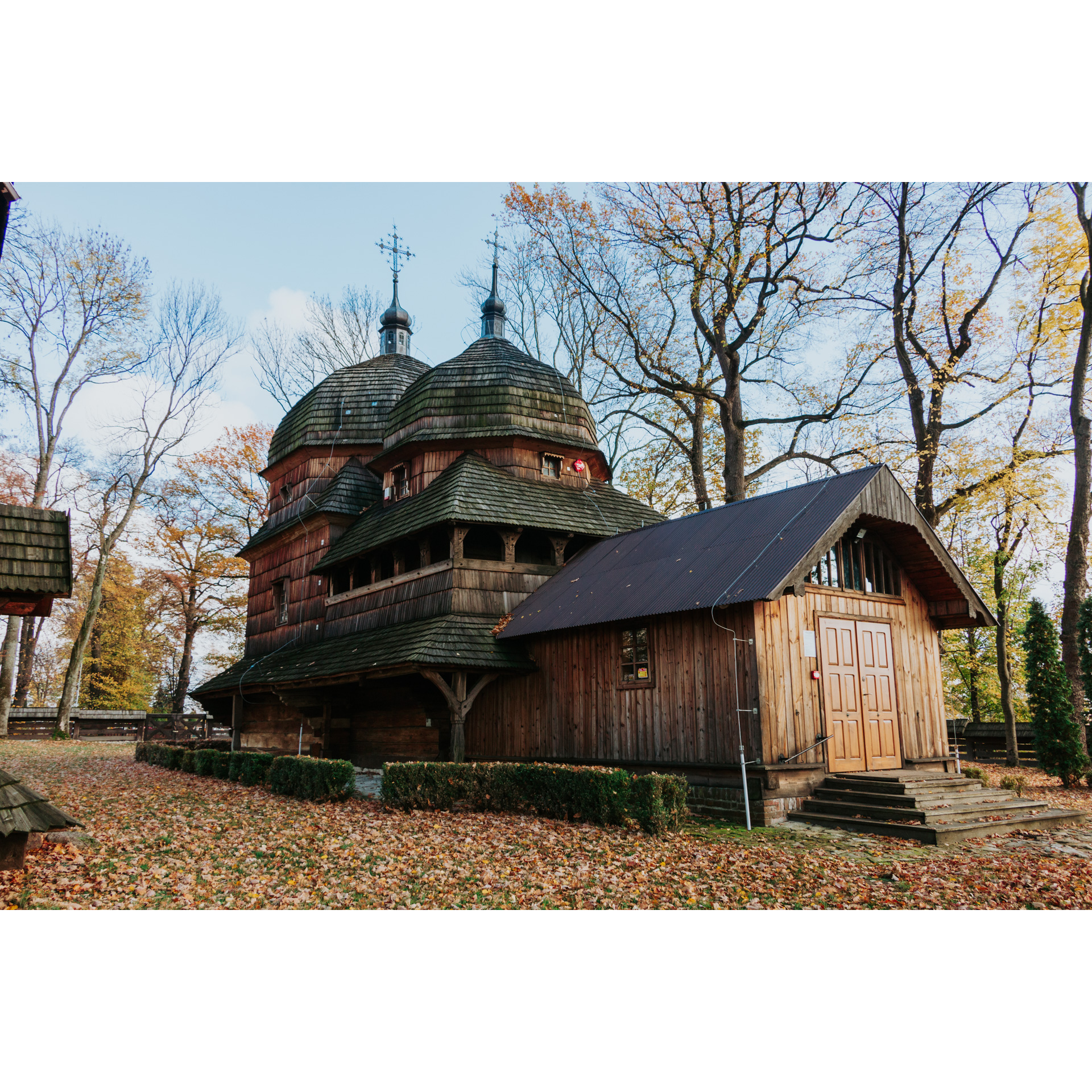 A wooden Orthodox church with domes and an added entrance to the temple against the background of trees
