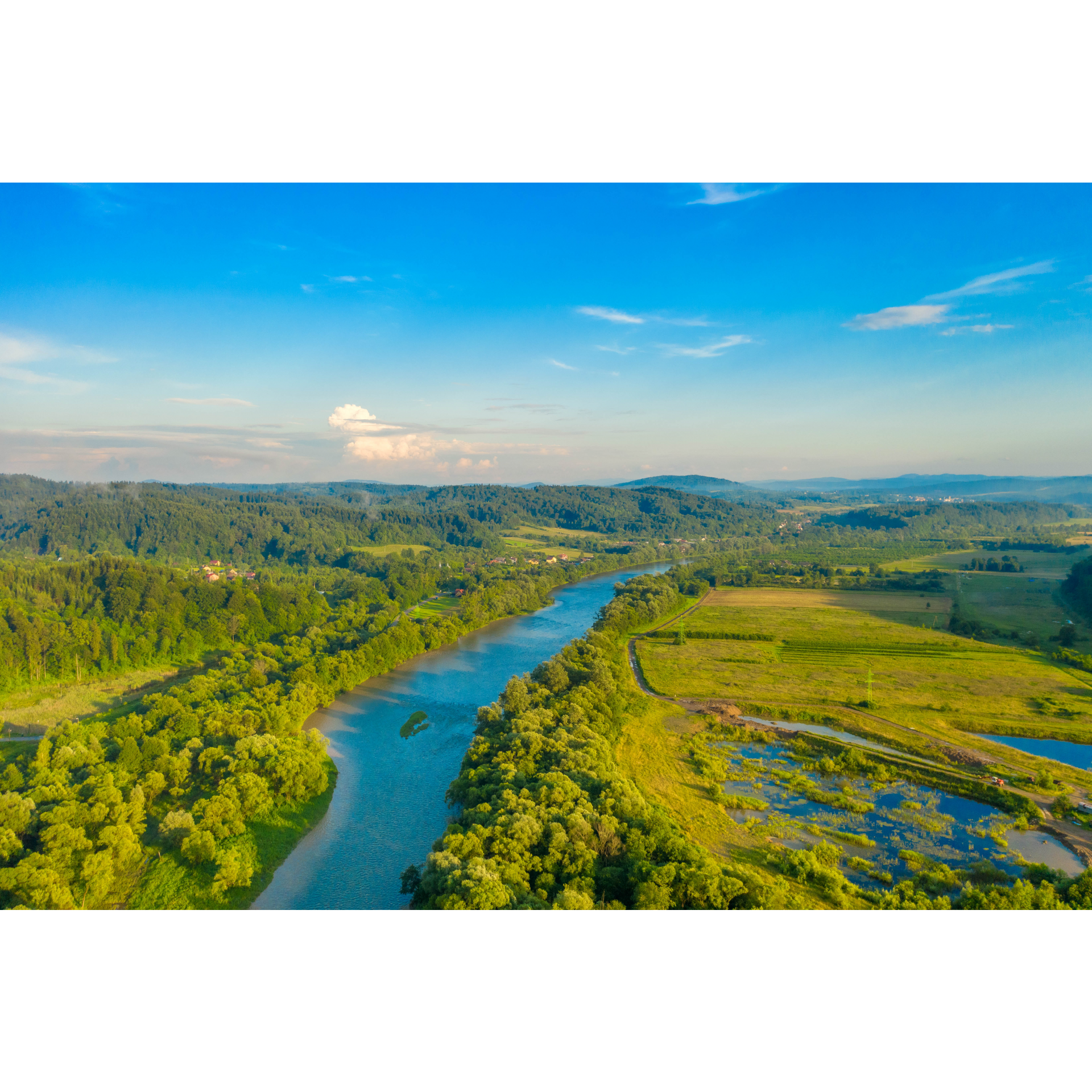 Aerial view of a long and wide river surrounded on both sides by green fields and forests