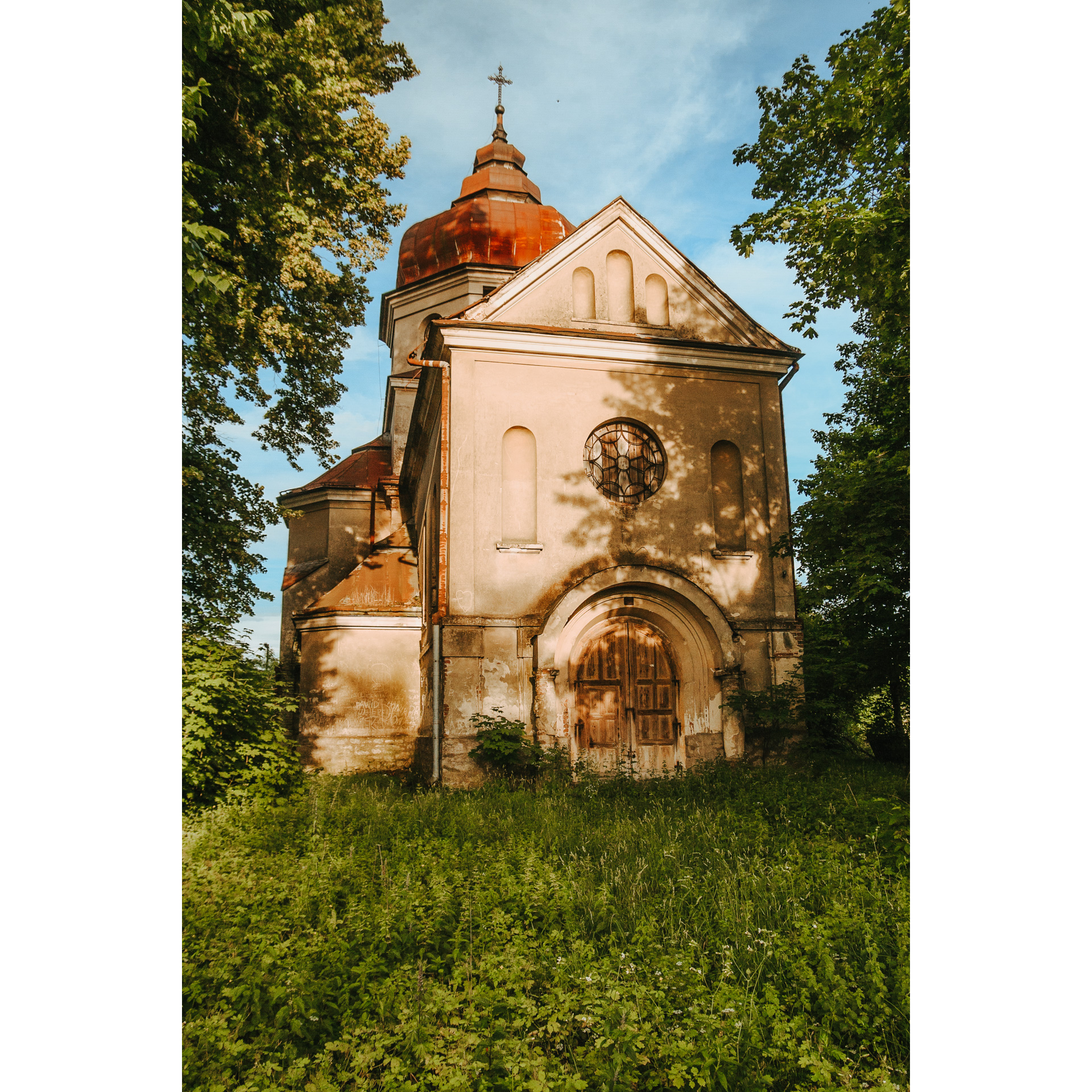 A bright, brick Orthodox church with a wooden door and a round stained-glass window