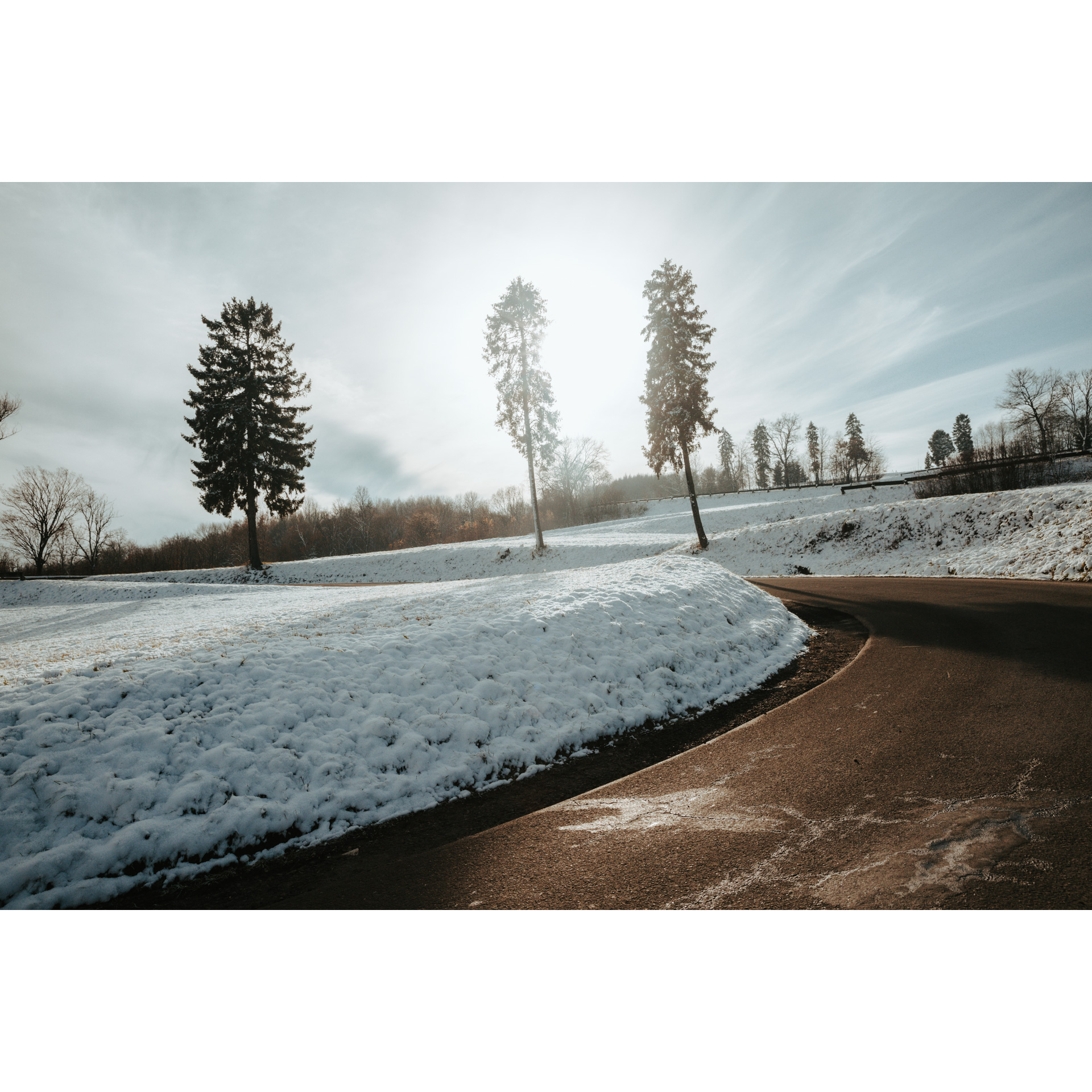 Asphalt road turning left with snow-covered shoulders