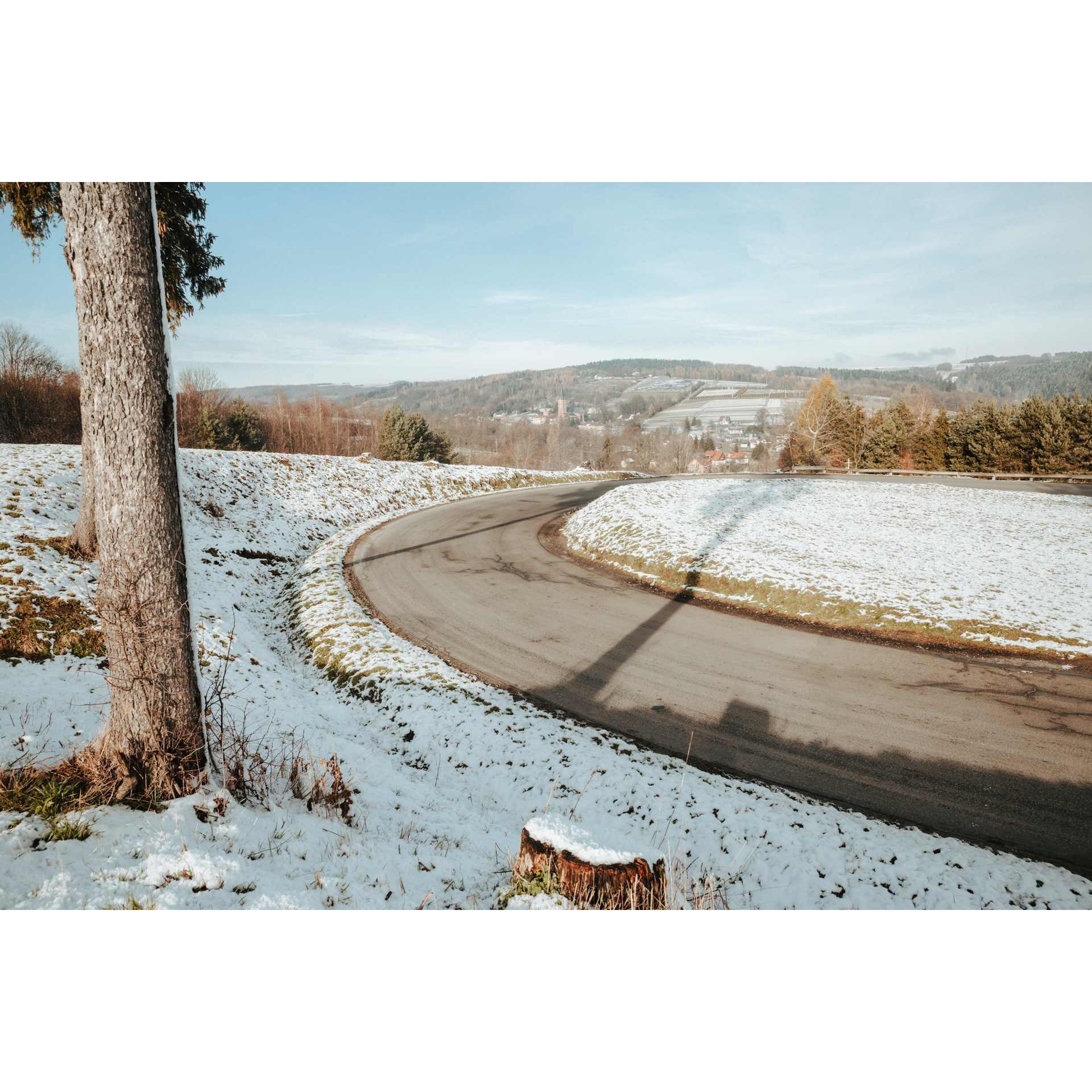 Asphalt road turning right with snow-covered shoulders against the background of hills