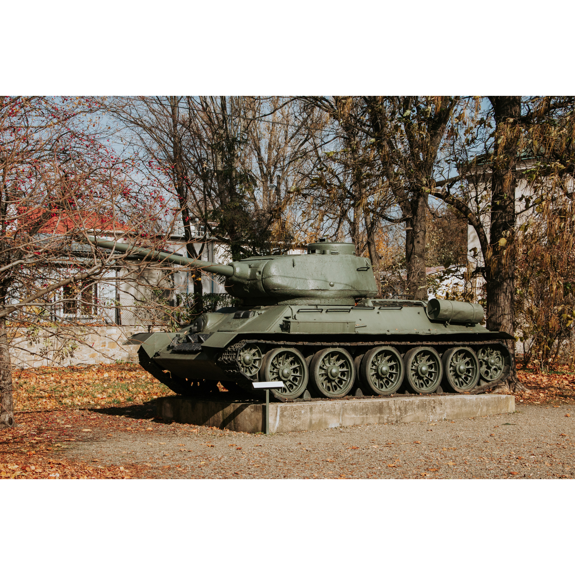A historic tank standing on a brick platform against the background of trees