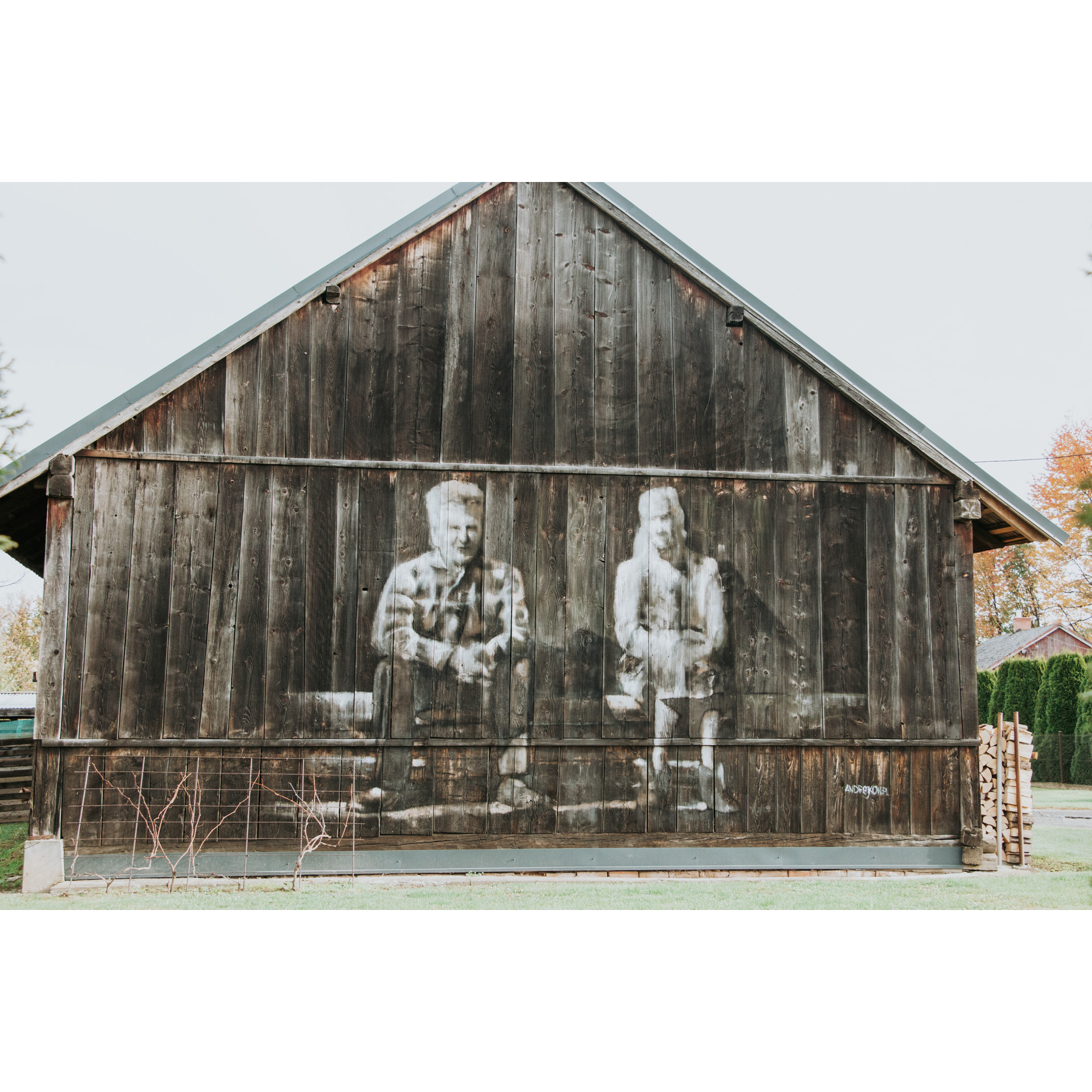 Black and white drawing on the wall of a wooden building showing a man in a plaid shirt and a woman in a headscarf sitting on a bench