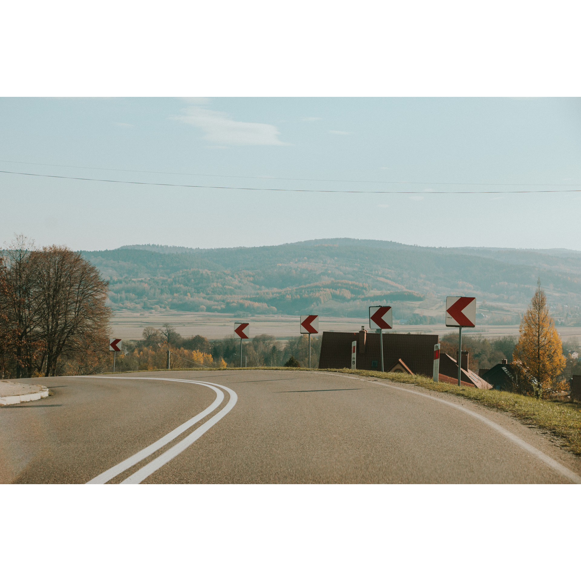 An asphalt two-lane road turning left against the backdrop of hills