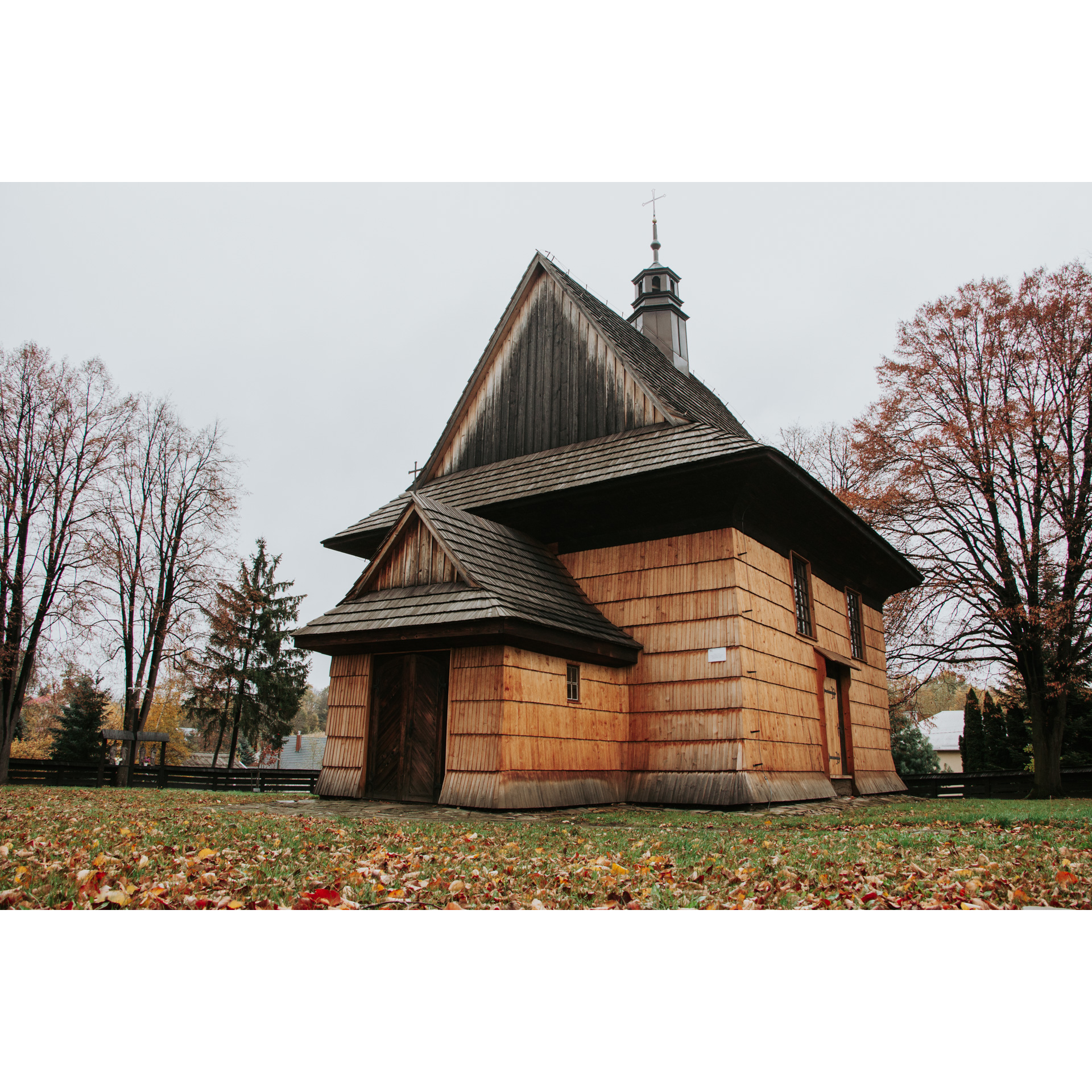Drewniany, zabytkowy kościół z jasnego drewna i z czarnym trójkątnym dachem, wieżyczką i krzyżem na szczycie