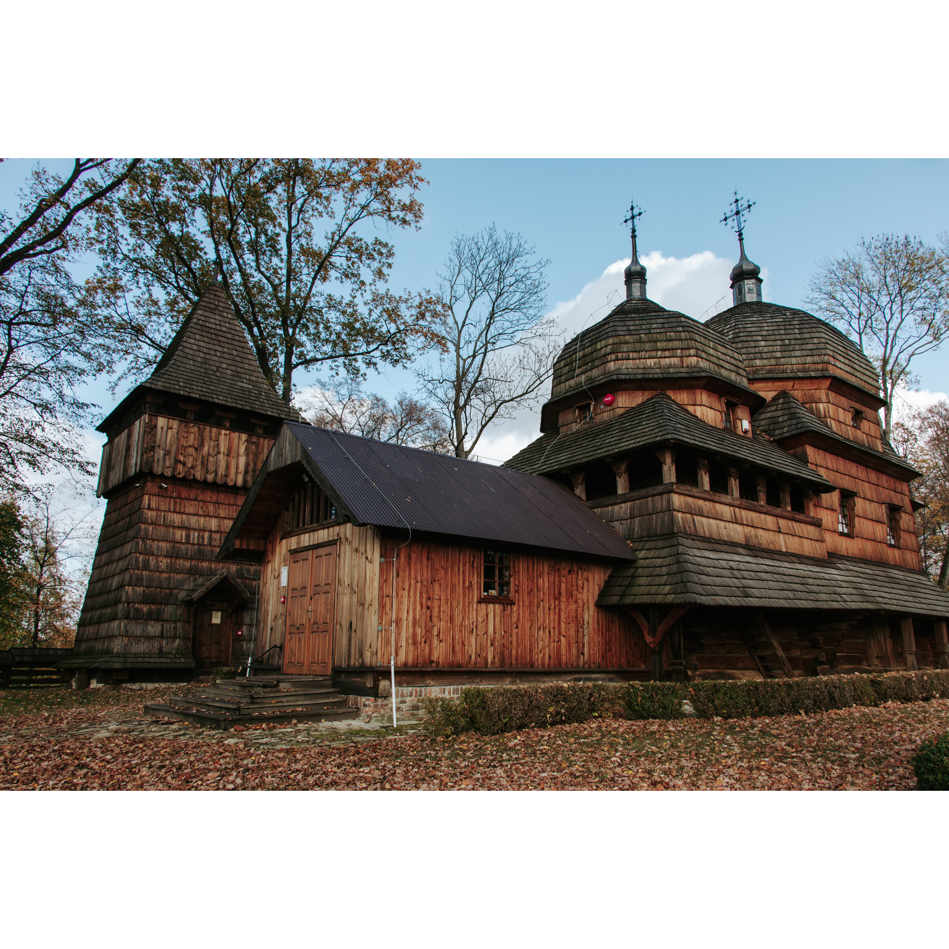 Wooden historic church with 2 towers with a domed roof and one tower with a pointed roof
