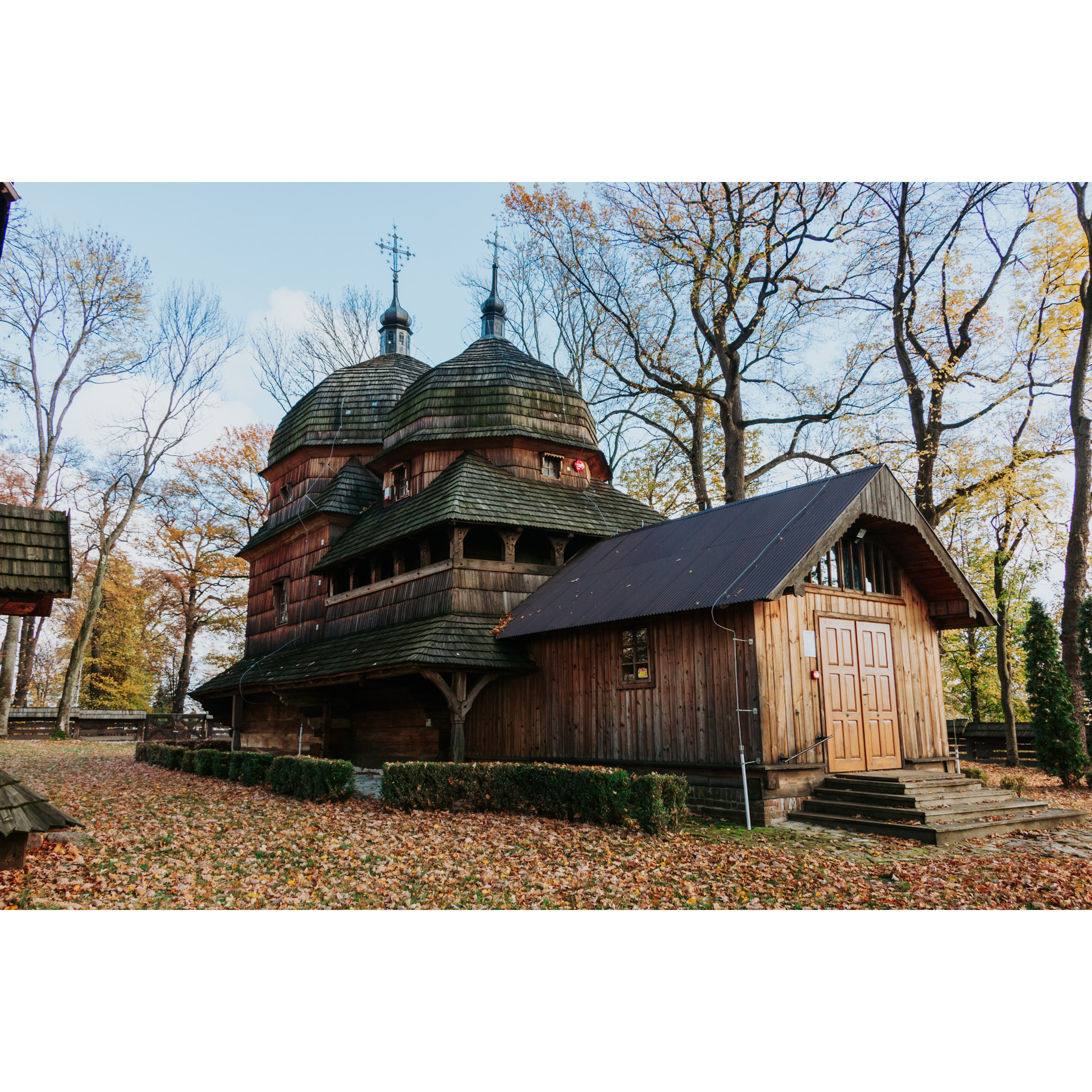 A wooden historic church with 2 towers with domed roofs topped with metal crosses