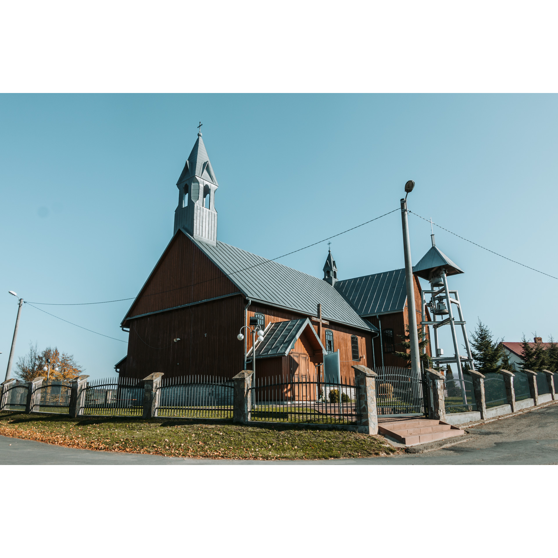 A wooden church with a roof made of sheet metal and a turret, and a belfry with two bells standing next to it