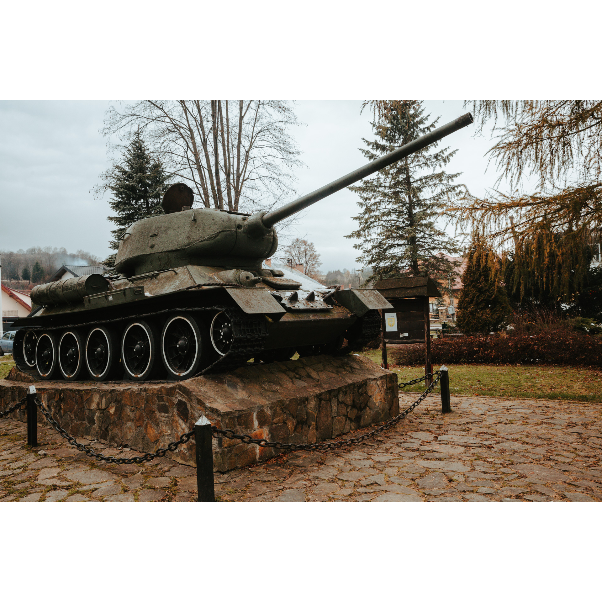 A green vintage tank standing on a brick platform with the barrel pointing to the right and up, surrounded by posts and a chain