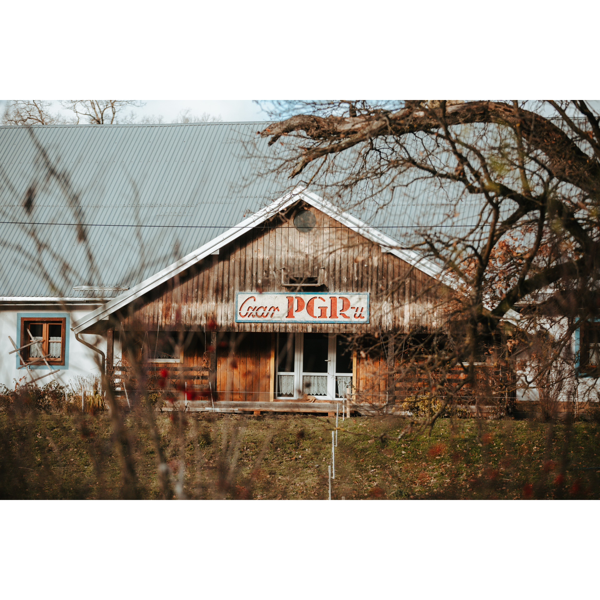 The wooden facade of the building with the "Czar PGR-u" signboard, with a gray tin roof