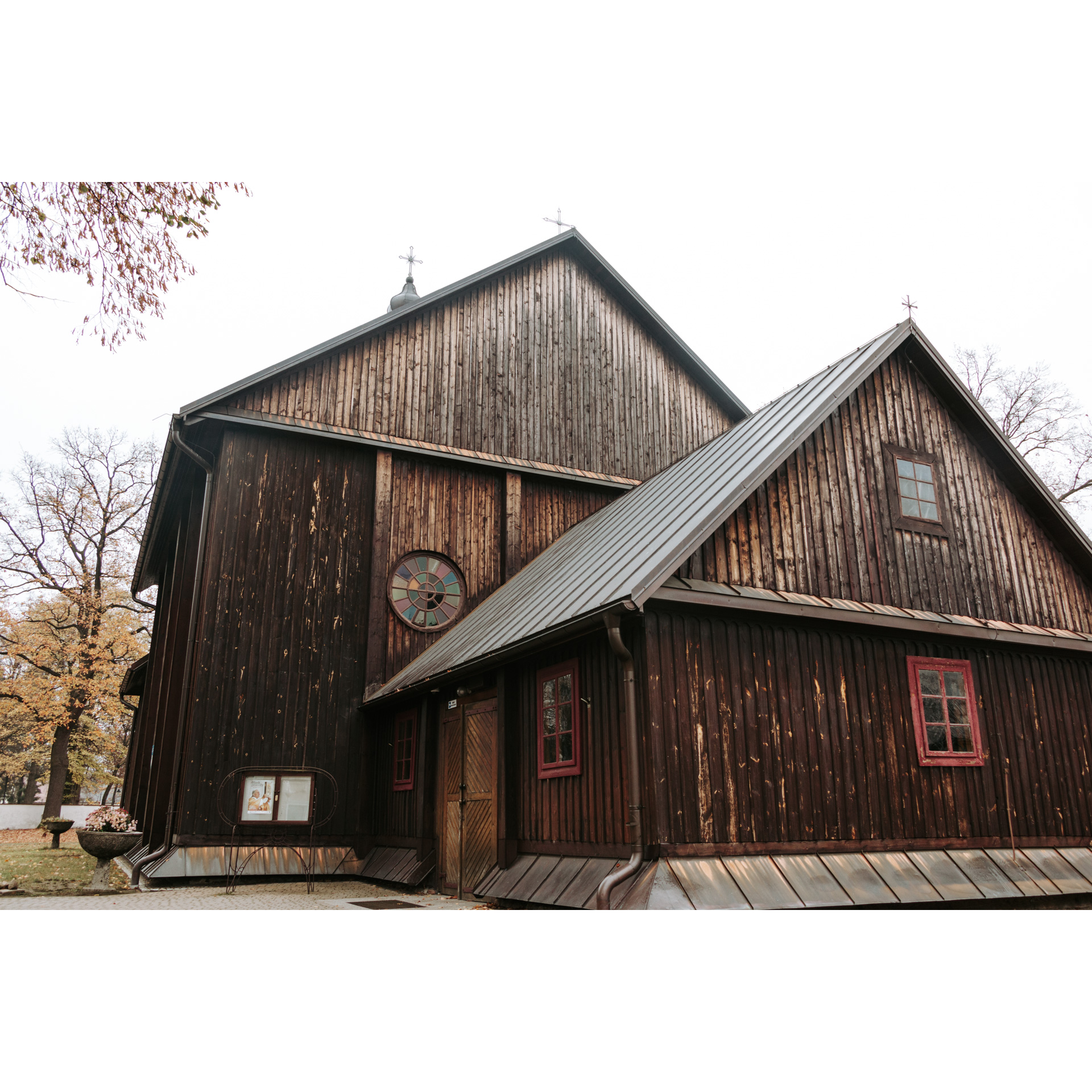 A dark brown wooden church with a sloping tin roof, a cross on top and three small windows