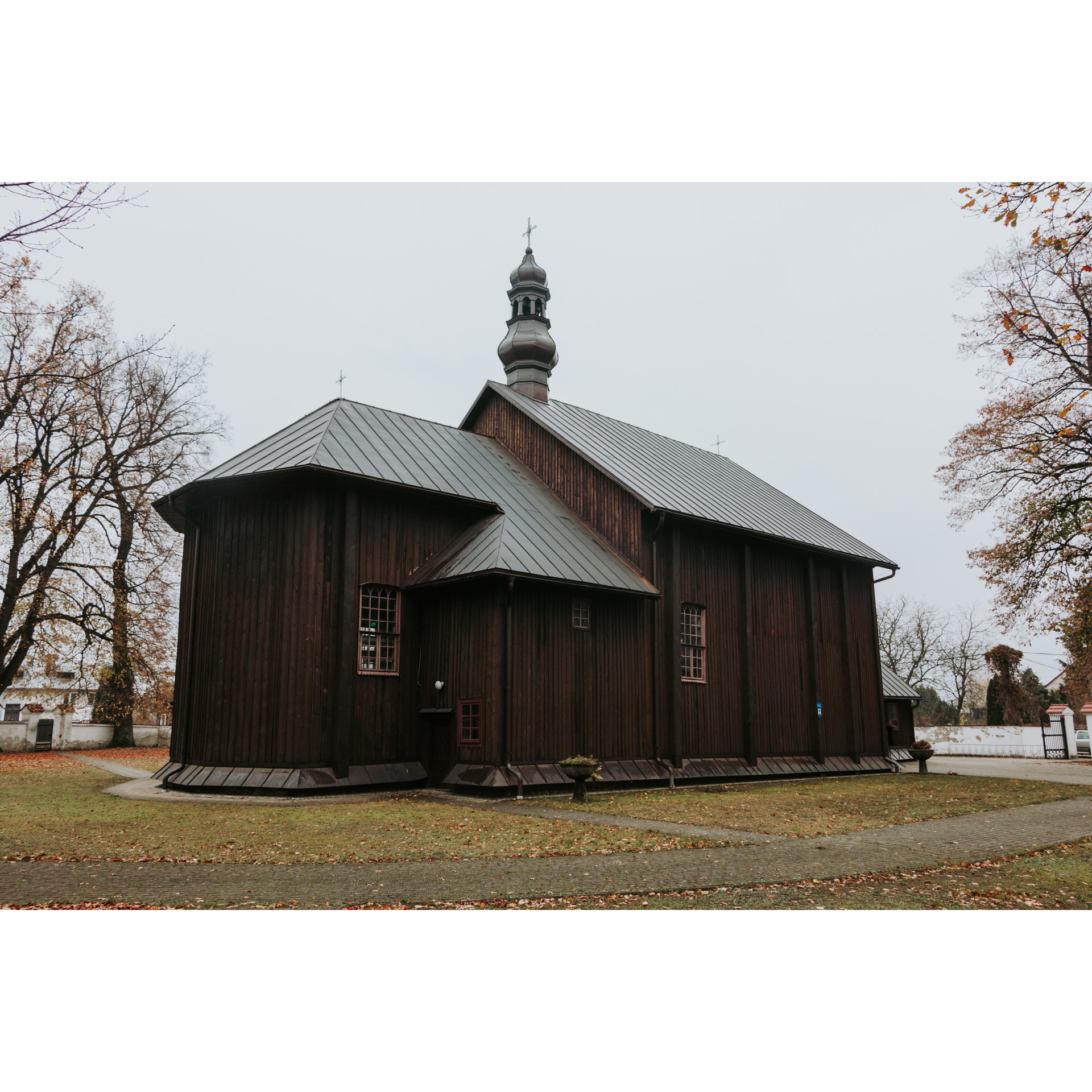 Ciemnobrązowy, drewniany kościół z blaszanym, spadzistym dachem i krzyżem na szczycie wieżyczki