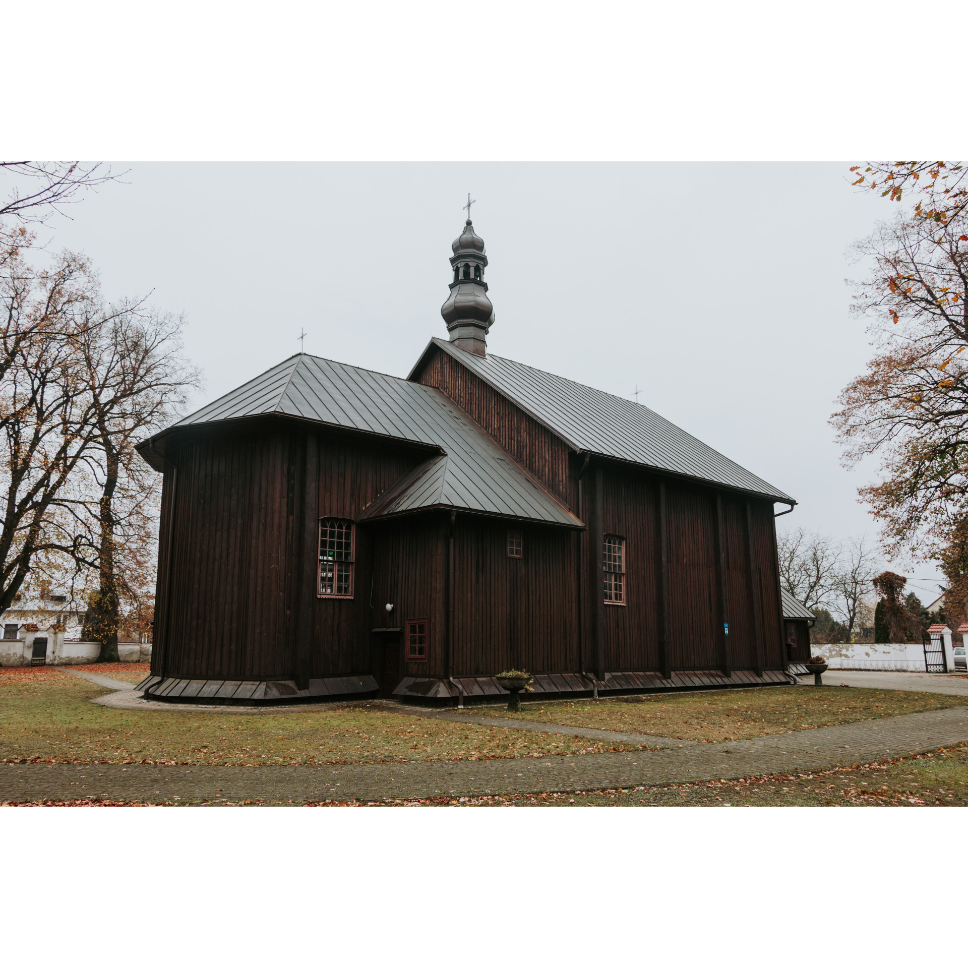 A dark brown, wooden church with a tin, sloping roof and a cross on top of the turret