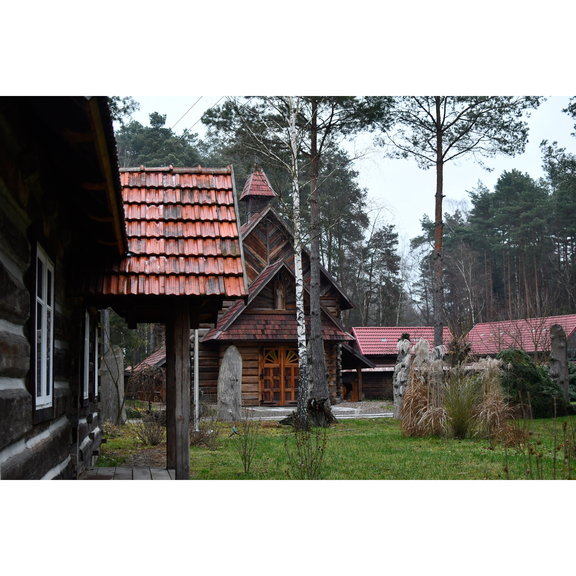 Drewniany kościół z wieżyczką i czerwonym dachem w otoczeniu drewnianych budynków i drzew