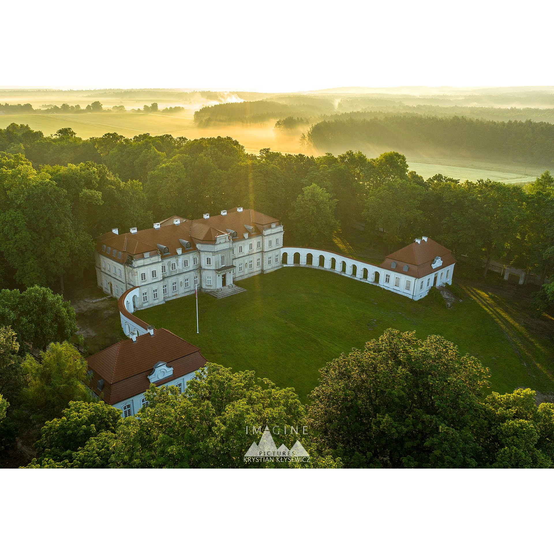 Widok na pałac Łosiów w Narolu z drona przy zachodzącym słońcu. Wokół dużo zieleni.